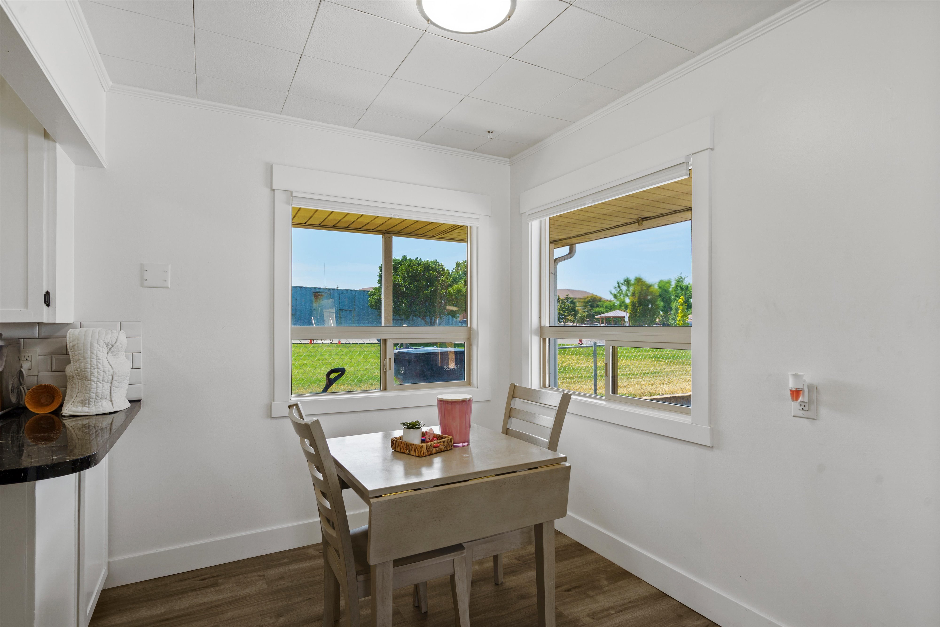 Dining area featuring two windows, wood-finish flooring, white trim, and a drop-leaf table