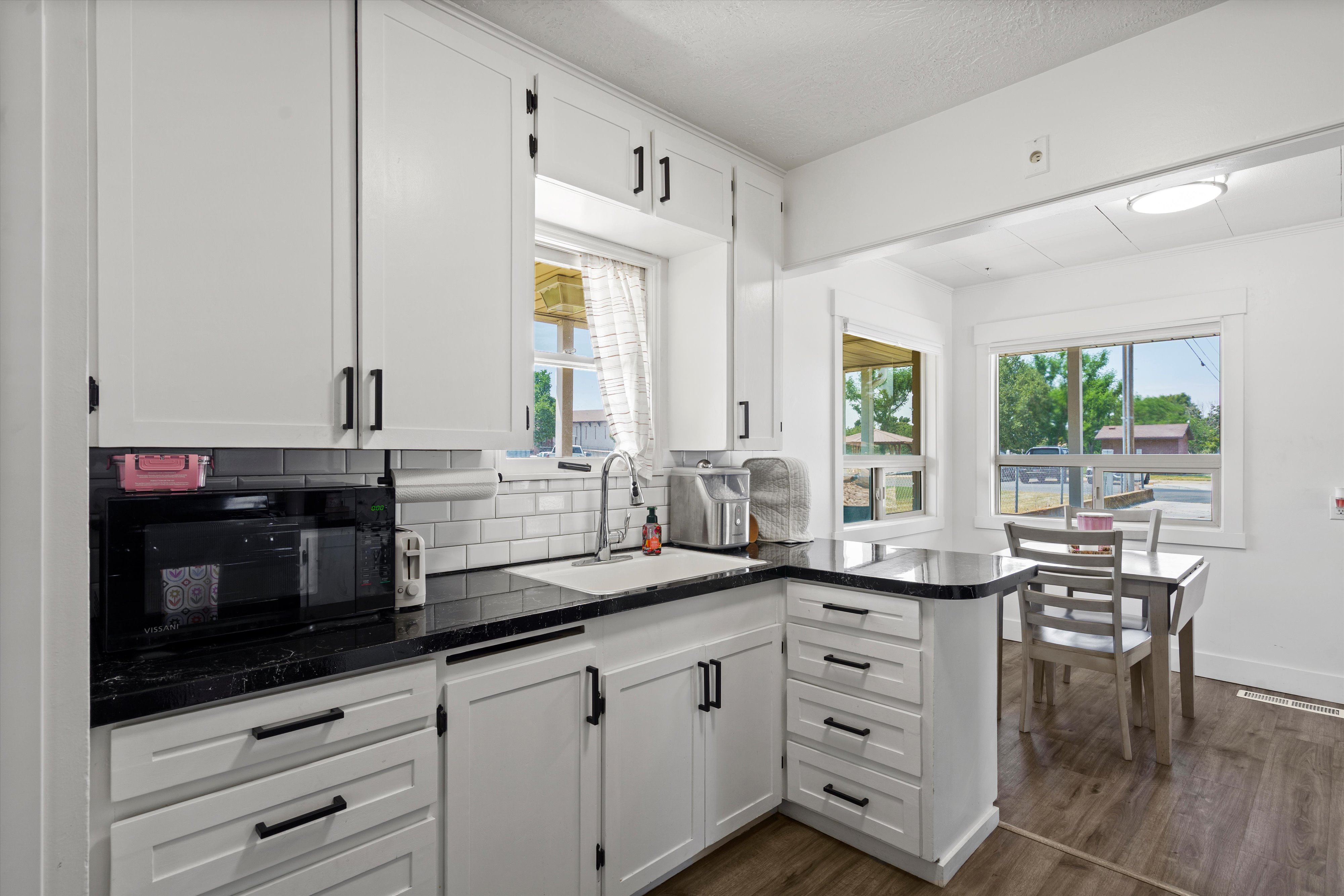 Kitchen featuring white shaker-style cabinetry with matte black hardware, dark stone countertops, and a white subway tile backsplash