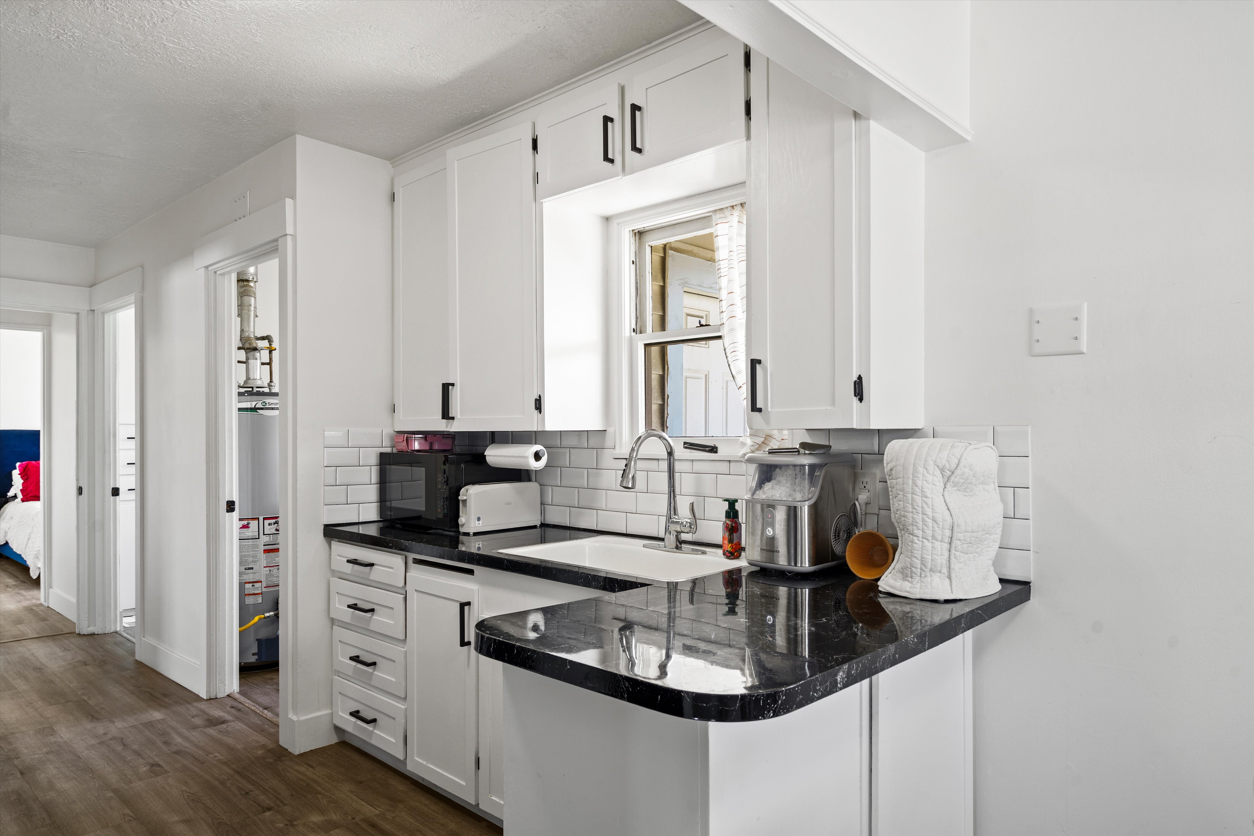 Kitchen featuring white cabinetry, dark countertops, a white subway tile backsplash, and a stainless steel faucet