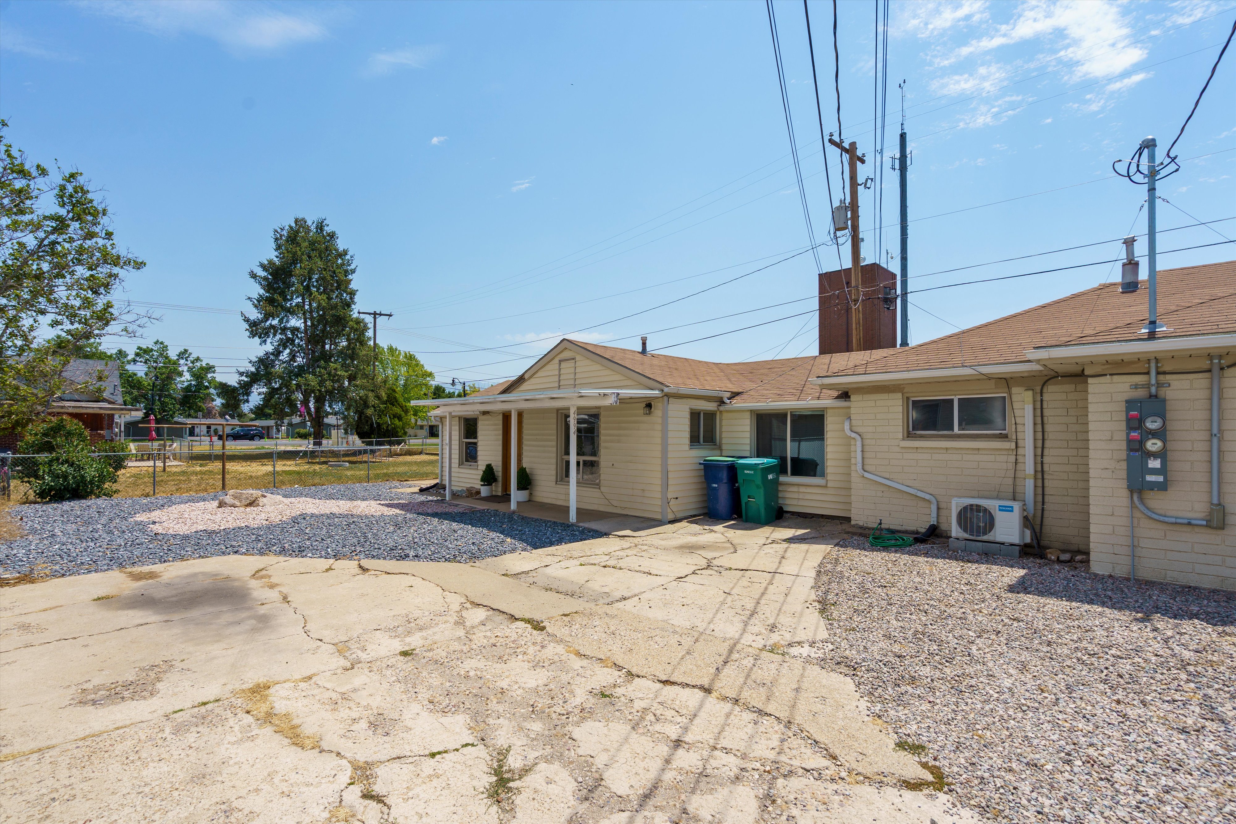 Rear exterior with a concrete patio, gravel landscaping, and mature trees