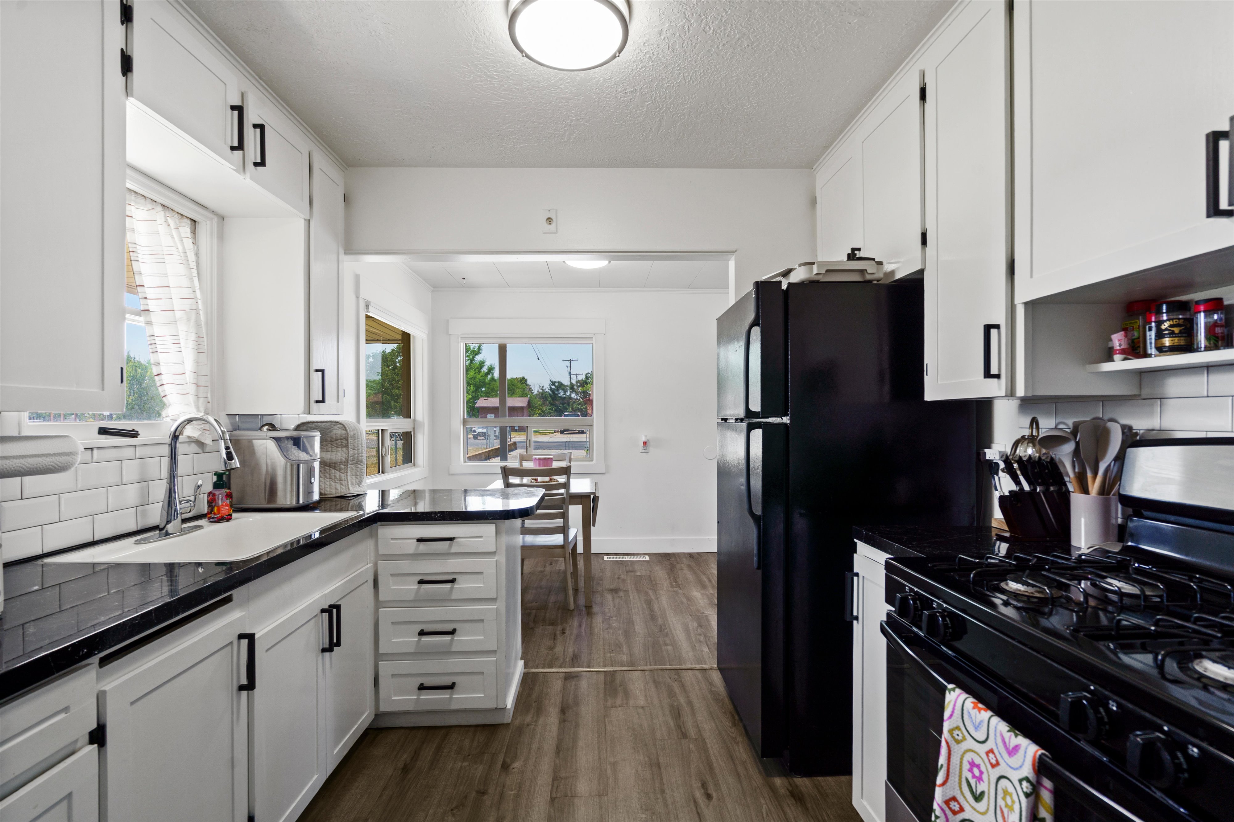 Galley kitchen featuring white cabinetry with matte black hardware, dark countertops, and a subway tile backsplash