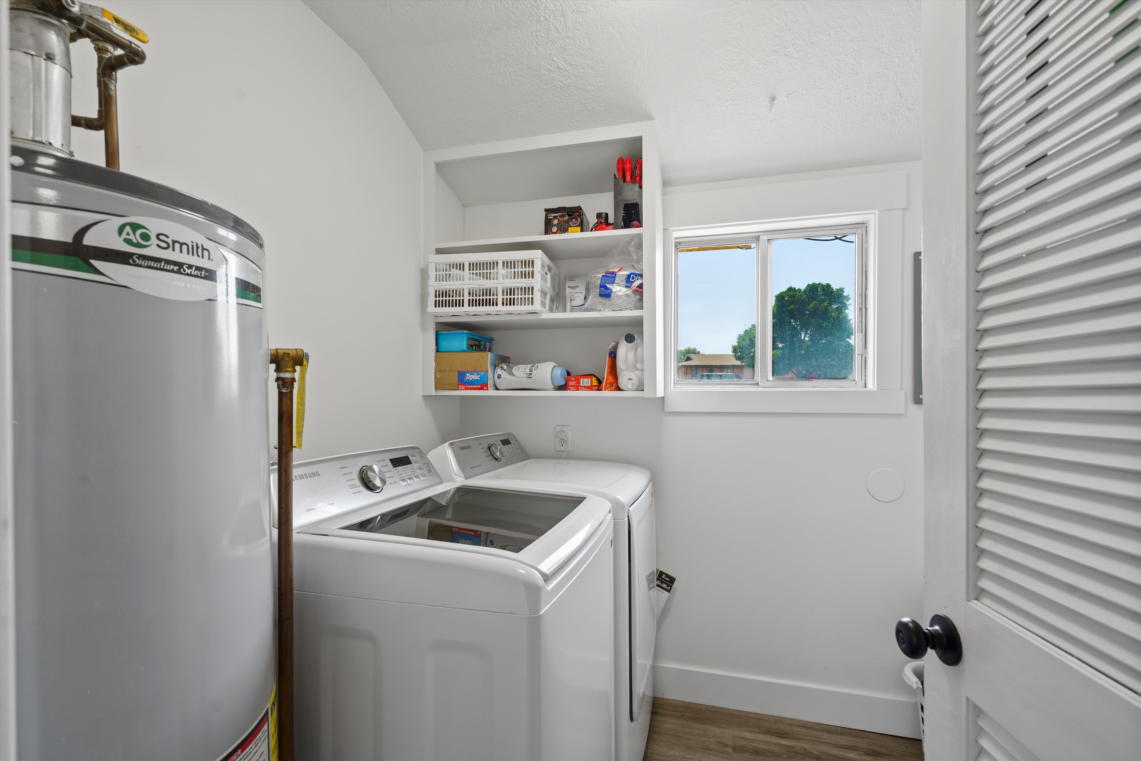 Dedicated utility area featuring a water heater, laundry appliances, a window, and built-in shelving