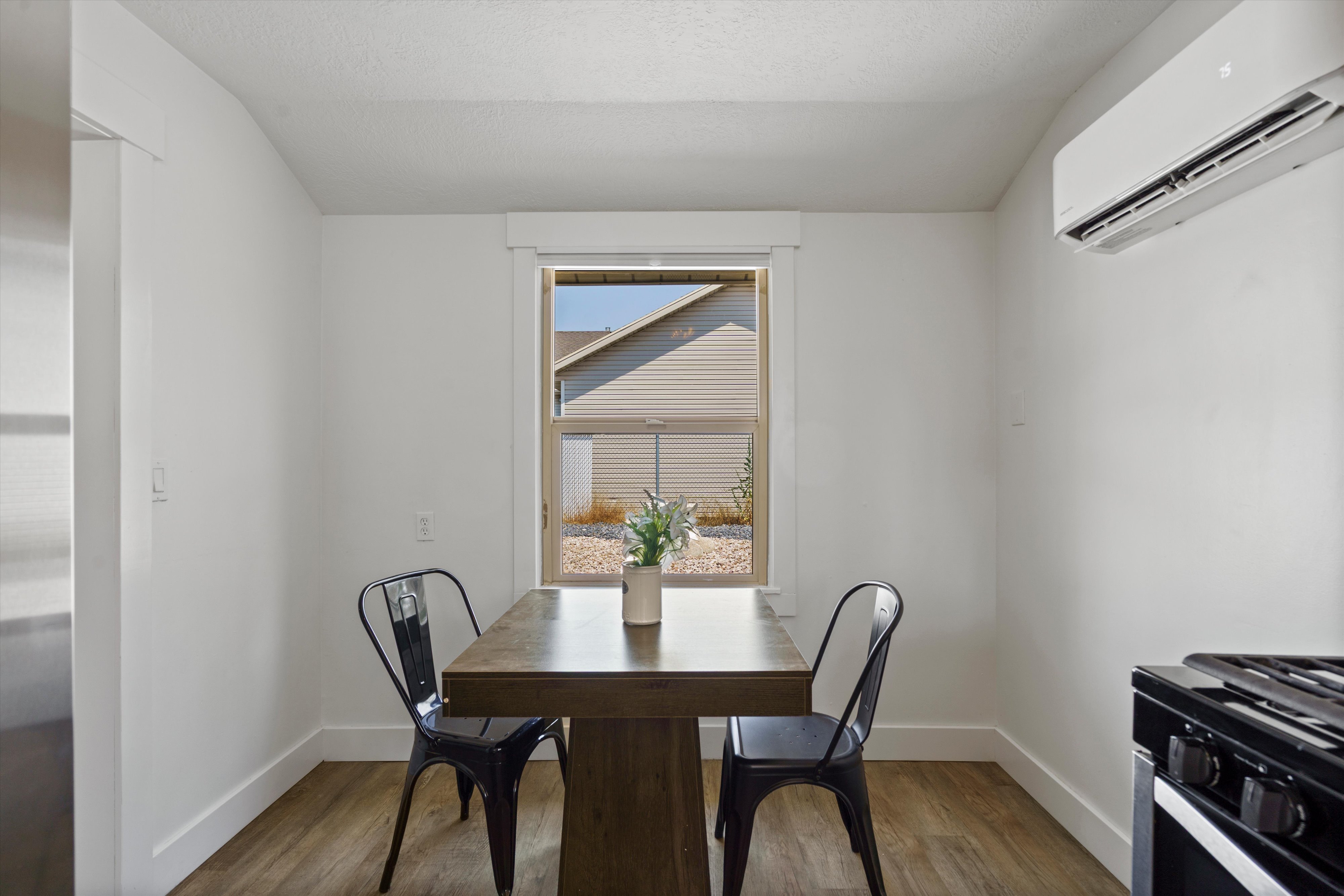 Compact dining area featuring a window with white trim, wood-finish flooring, and a wall-mounted air conditioning unit