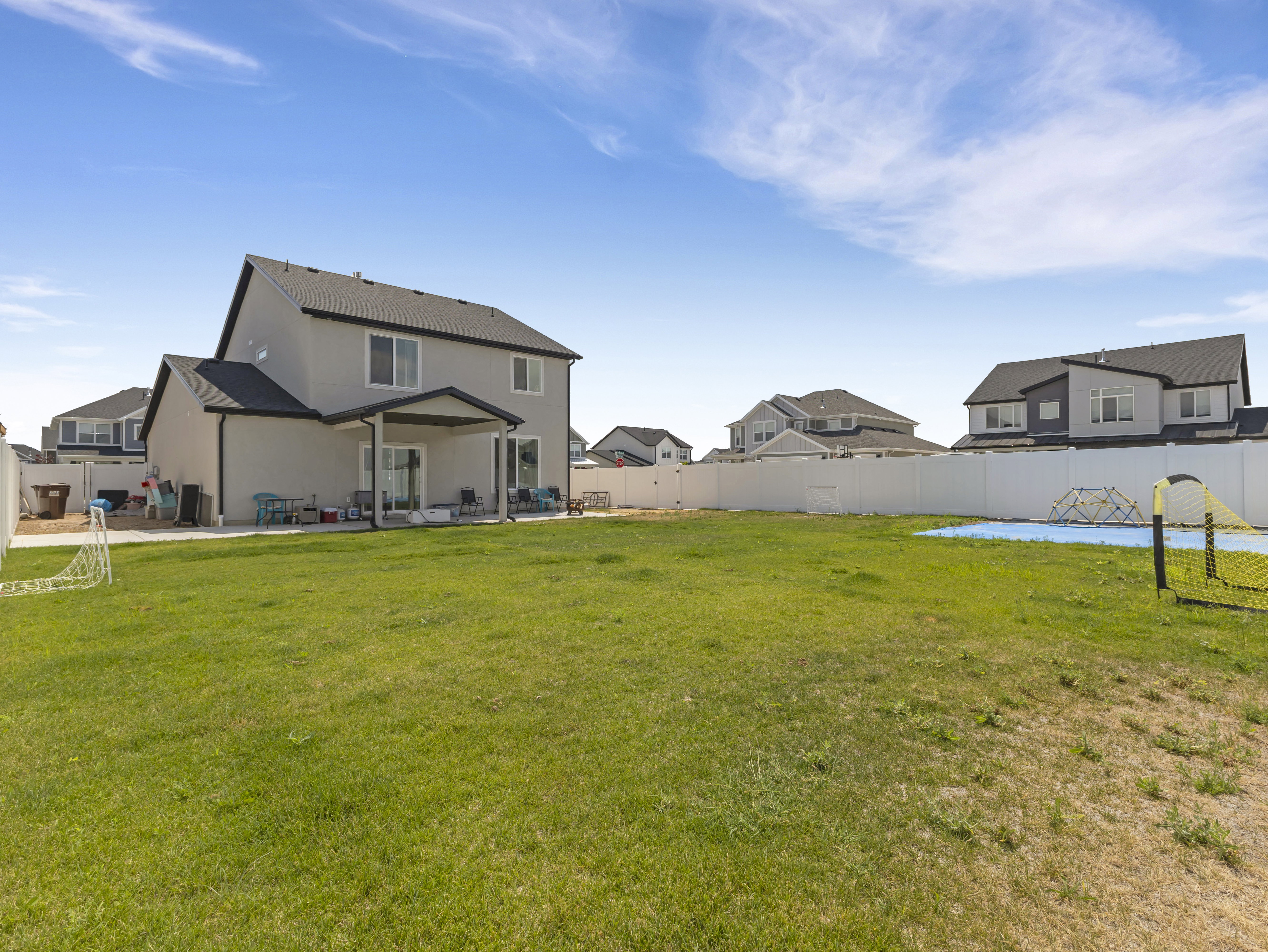 Expansive backyard featuring a manicured lawn, full vinyl privacy fencing, and a covered concrete patio