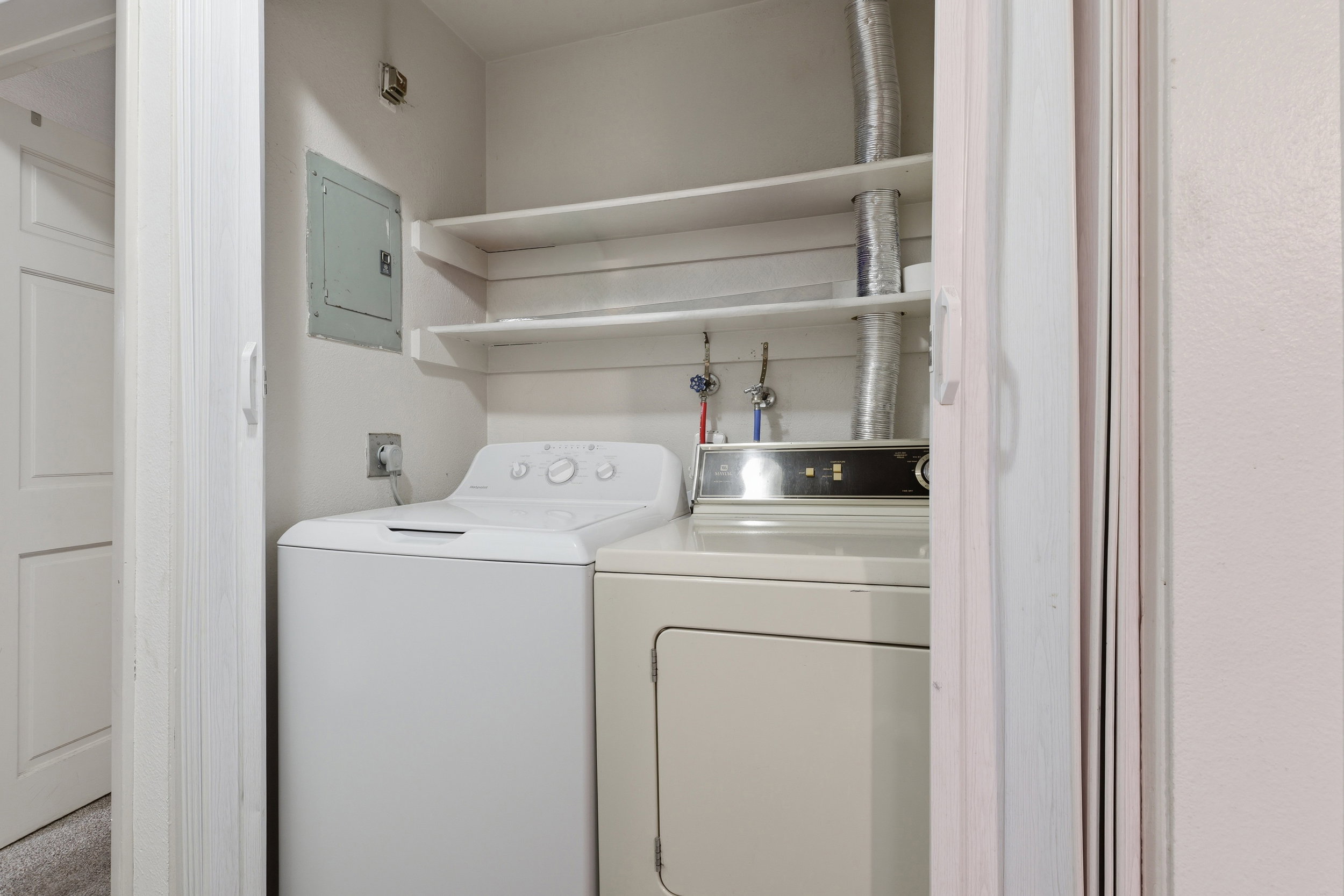 Dedicated laundry closet featuring a top-loading washing machine, front-loading dryer, and two built-in storage shelves