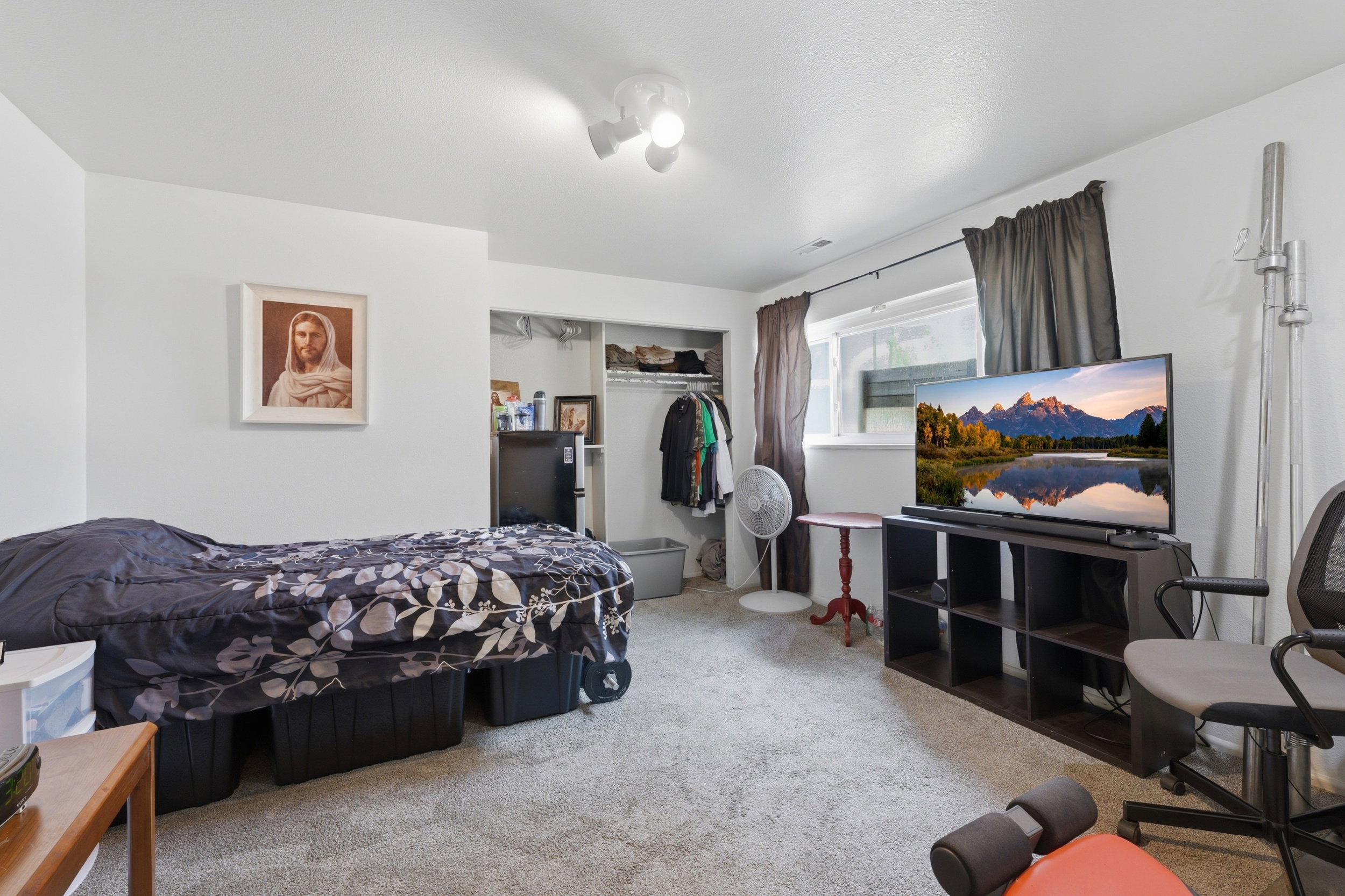 Carpeted room with white walls, a single window with dark drapes, and an open closet