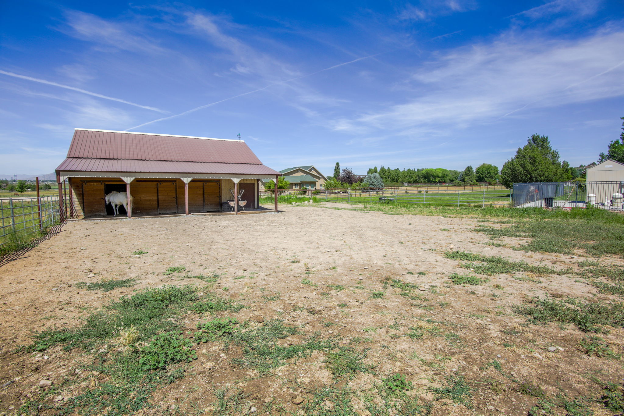 Barn structure featuring a brown metal roof, covered porch, multiple stalls, and a fenced enclosure