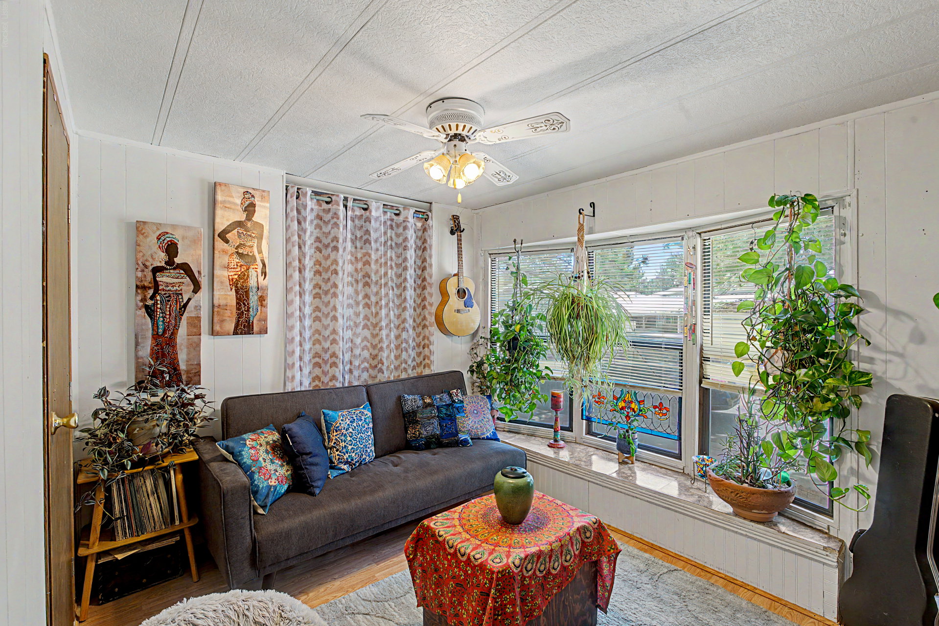 Living area featuring white paneled walls, a ceiling fan with integrated lighting, and multiple windows with horizontal blinds