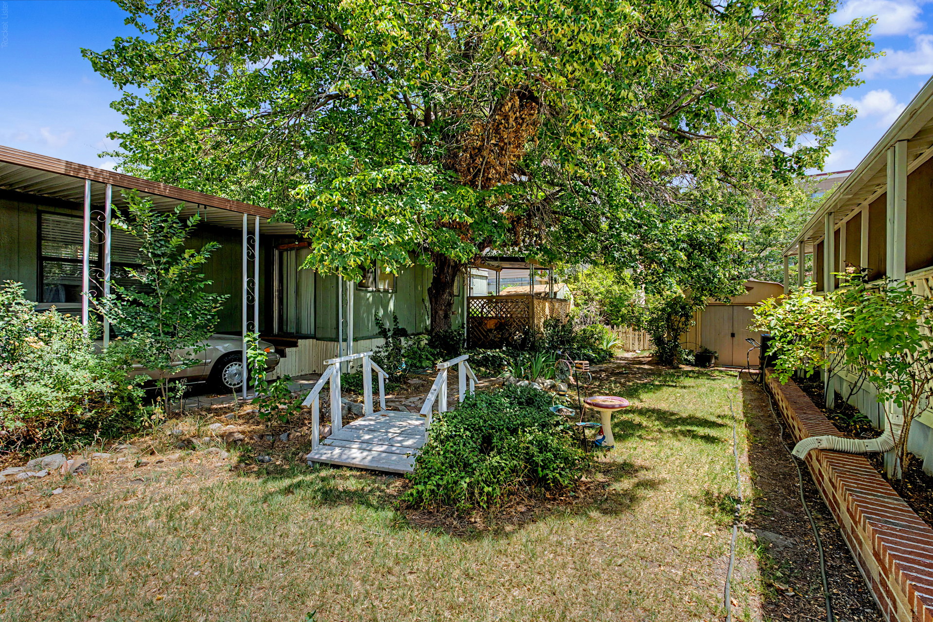 Shaded backyard featuring mature trees, a wooden bridge, and a storage shed