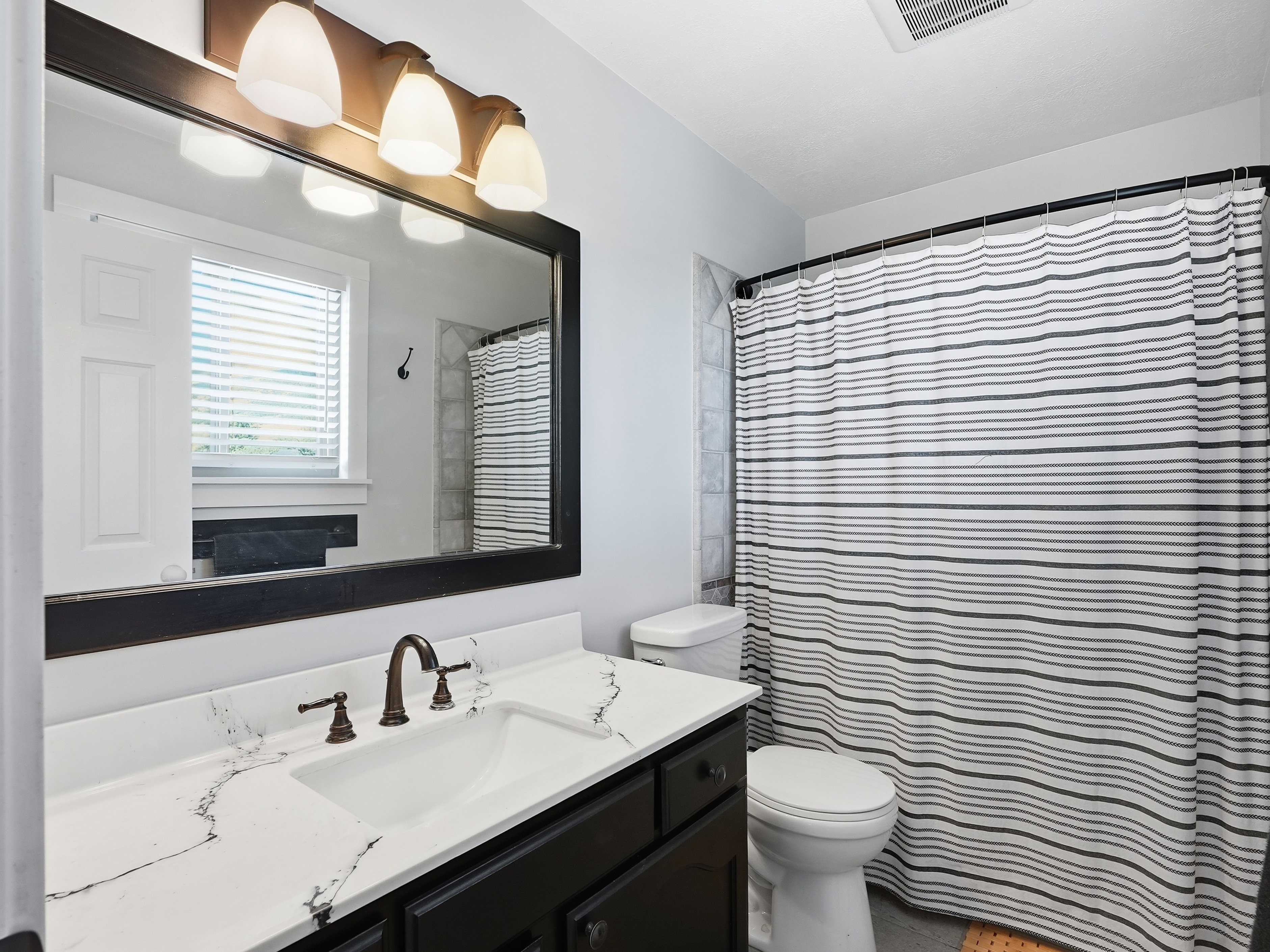 Bathroom vanity featuring a dark wood-finish cabinet with bronze hardware, a white countertop with grey veining, and an undermount sink