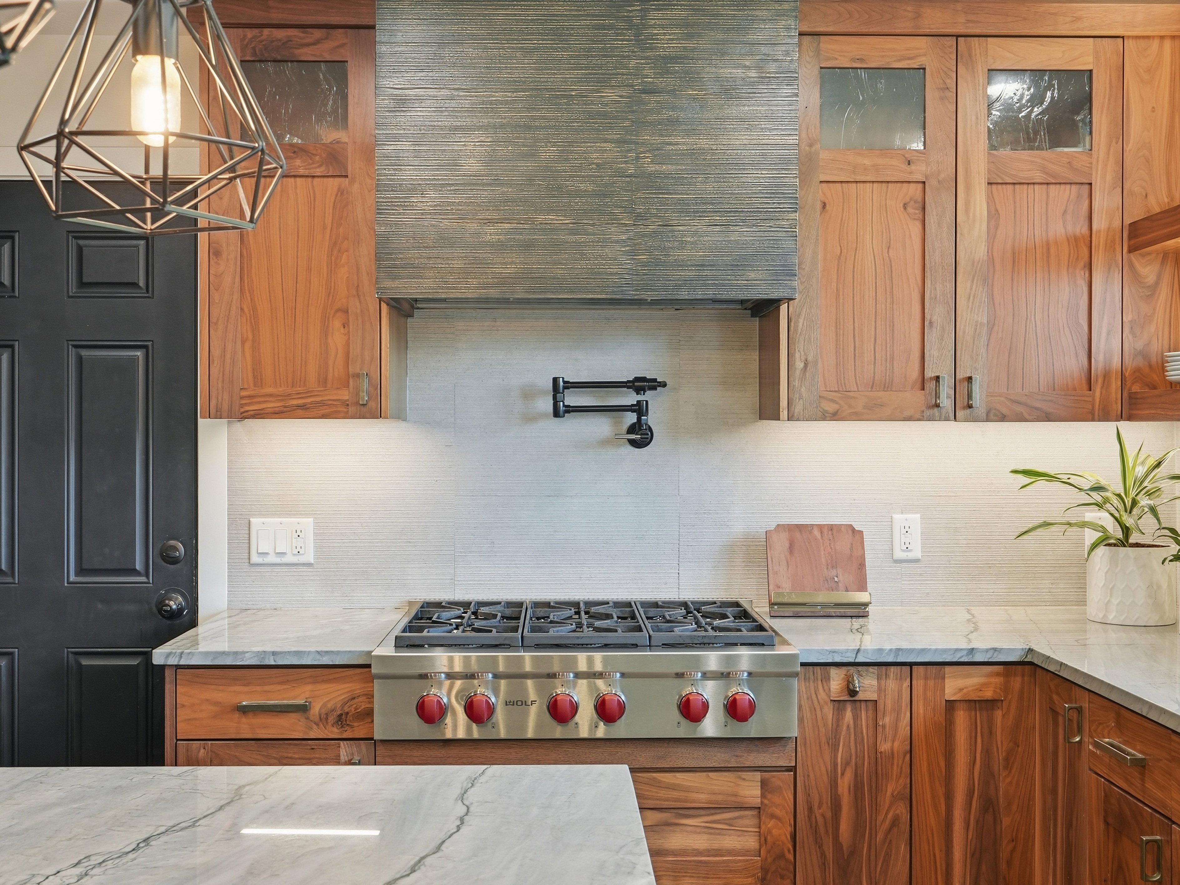 Gourmet kitchen featuring a stainless steel gas range with red knobs, a pot filler, wood-finish cabinetry, light-toned backsplash tiling, and stone countertops
