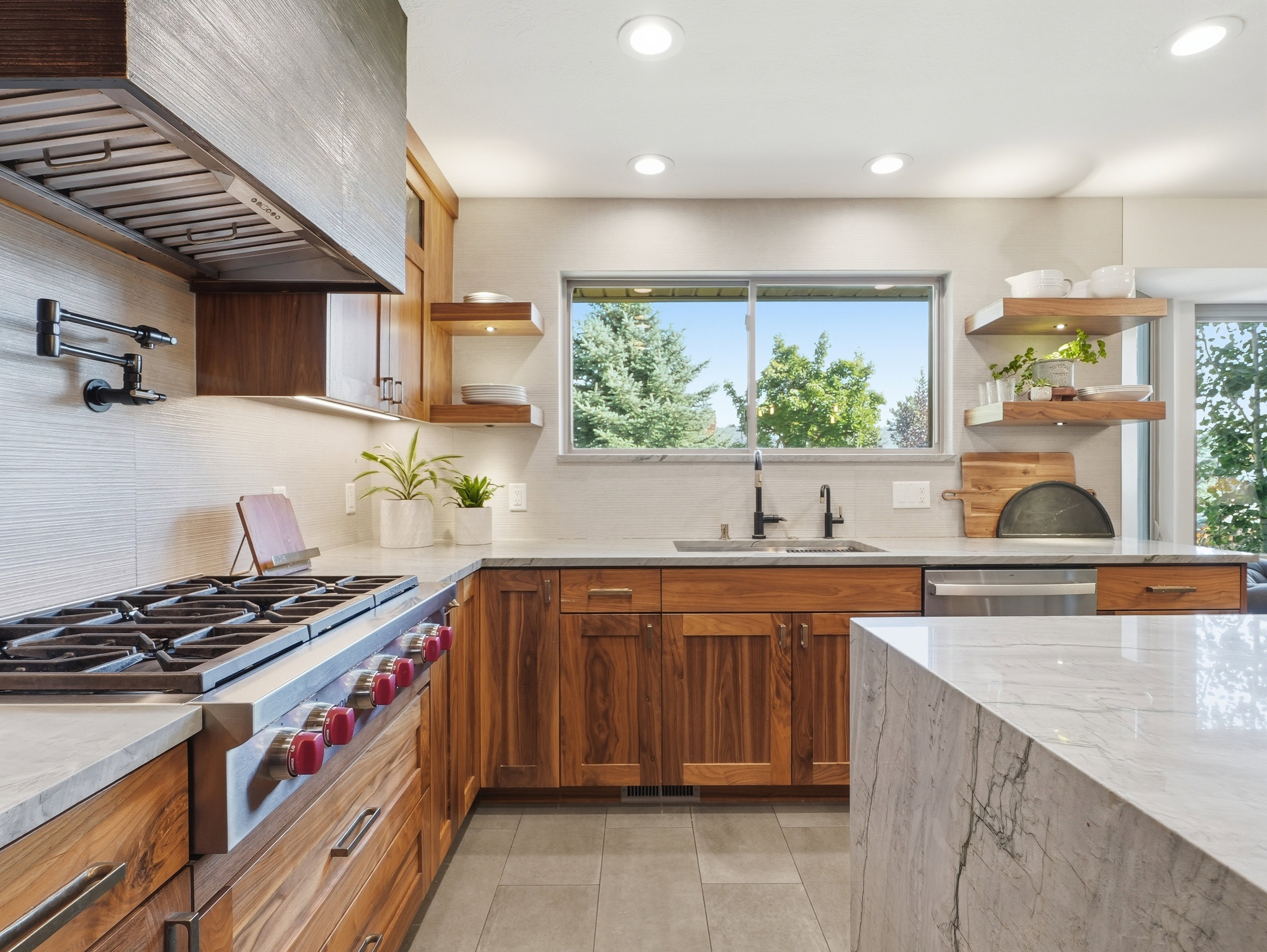 Gourmet kitchen with professional-grade range, built-in range hood, natural wood cabinetry, light-toned stone countertops, and recessed lighting