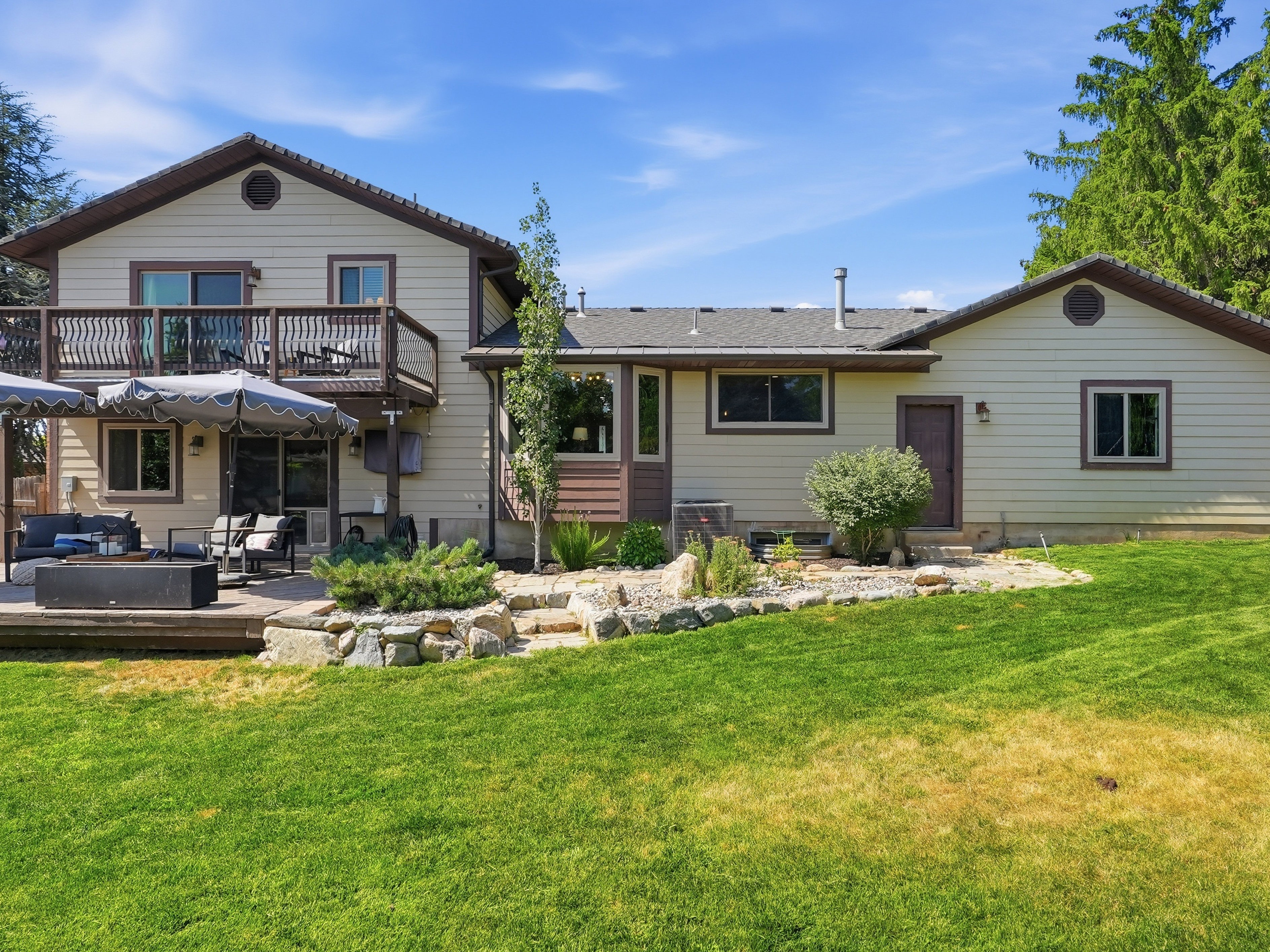 Spacious rear exterior featuring a two-story design with a second-level balcony, a ground-level patio, and extensive lawn space
