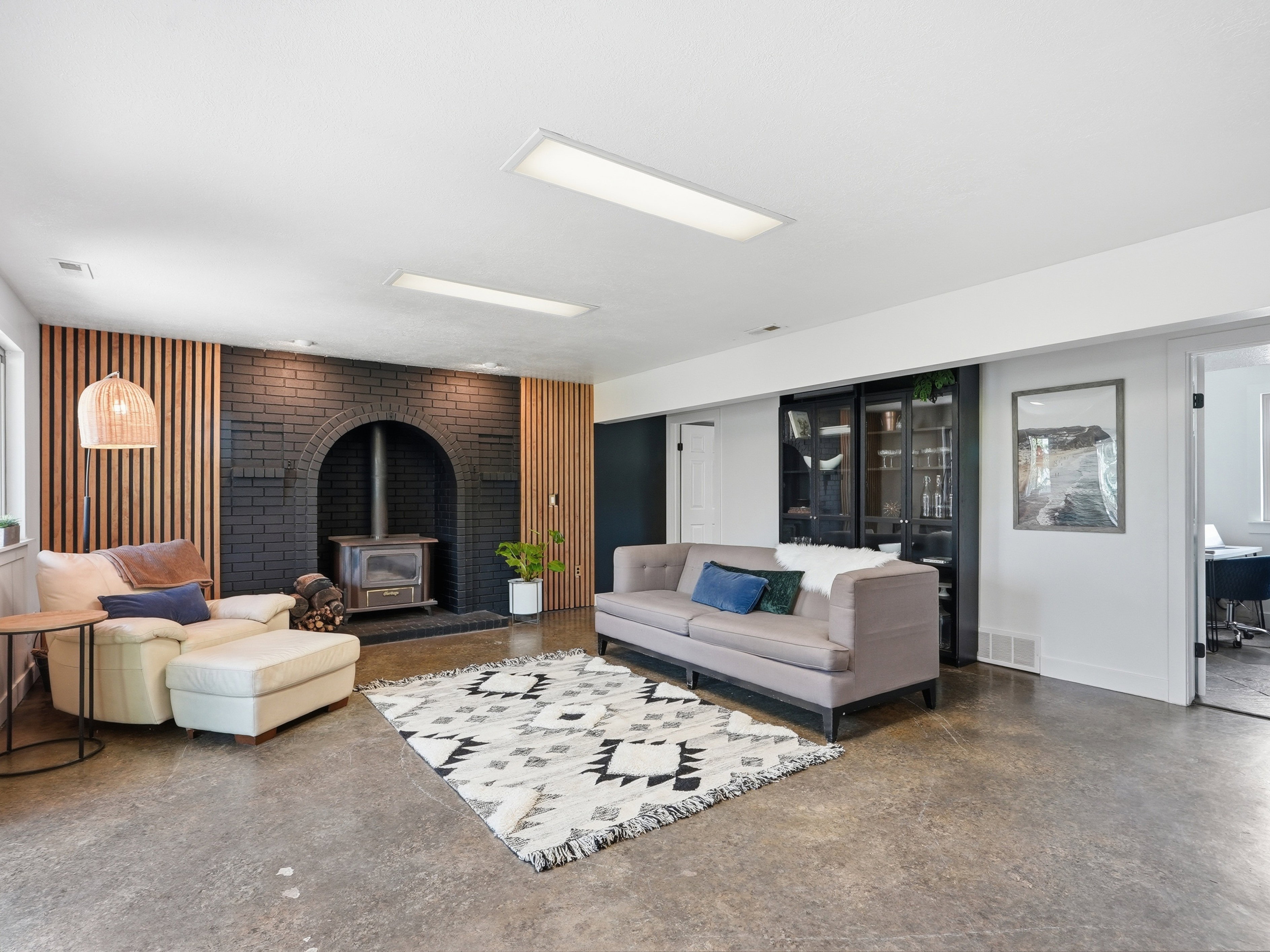 Spacious room featuring a black brick archway with a wood-burning stove, wood slat accent walls, and concrete flooring