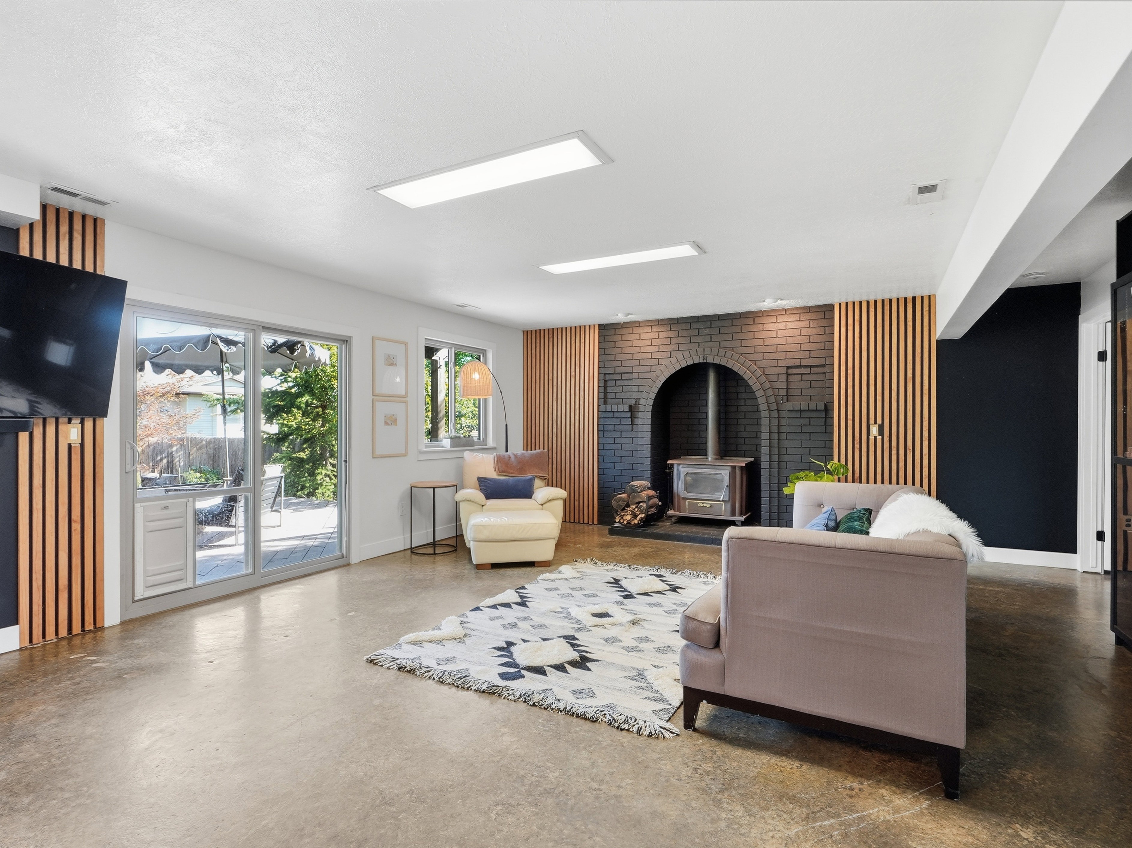 Spacious living area featuring concrete flooring, a black brick fireplace with a wood-burning stove, and wood slat accent walls