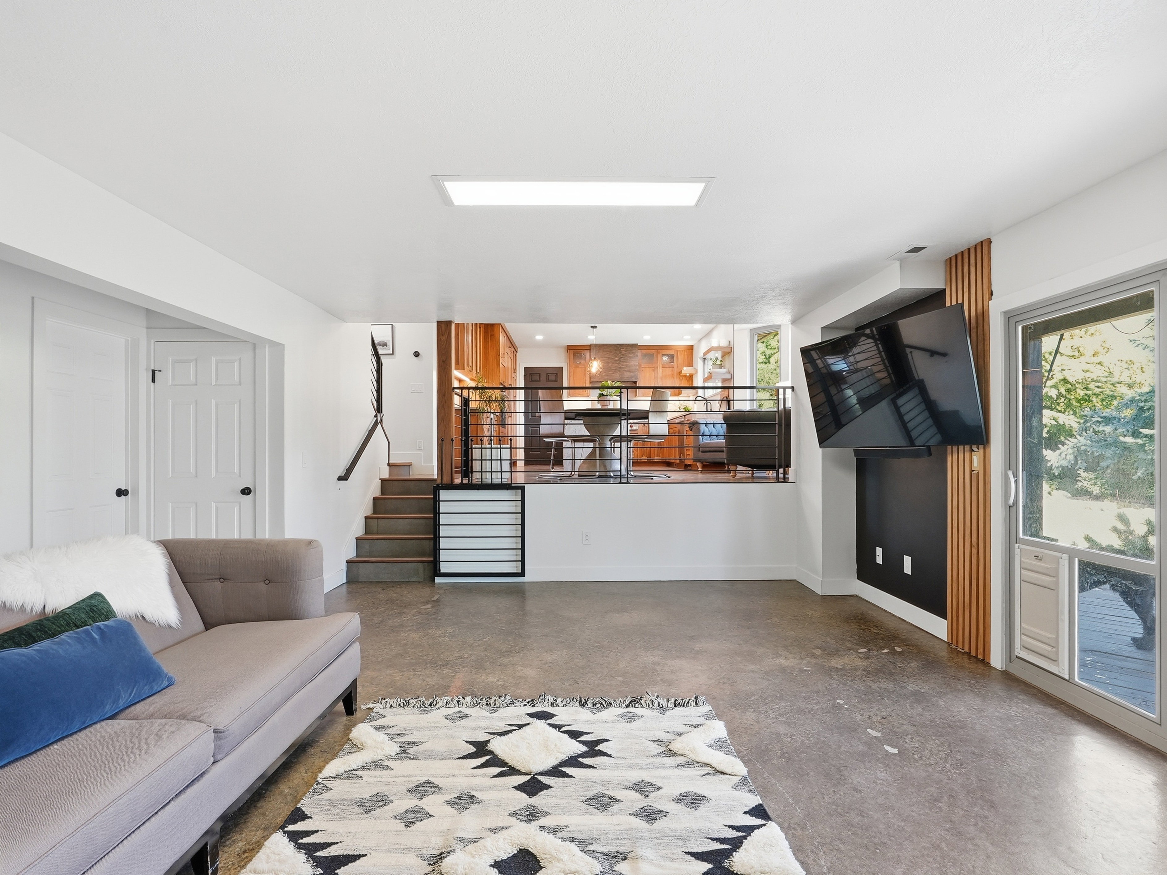 Lower-level living area featuring polished concrete flooring, a staircase with metal railings, and a built-in media wall with vertical wood accents