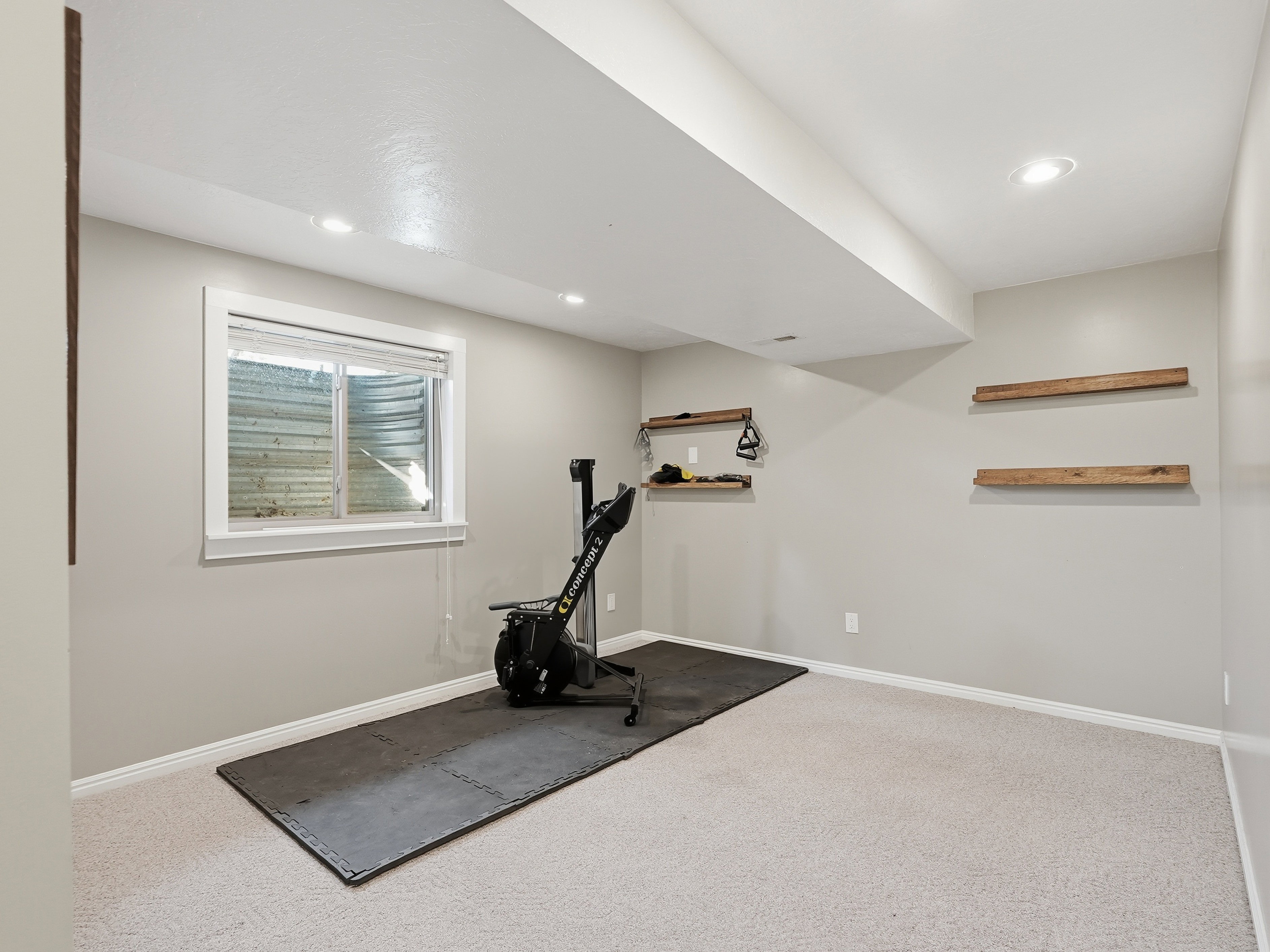 Carpeted room featuring a white-trimmed window, recessed lighting, and floating wood shelves