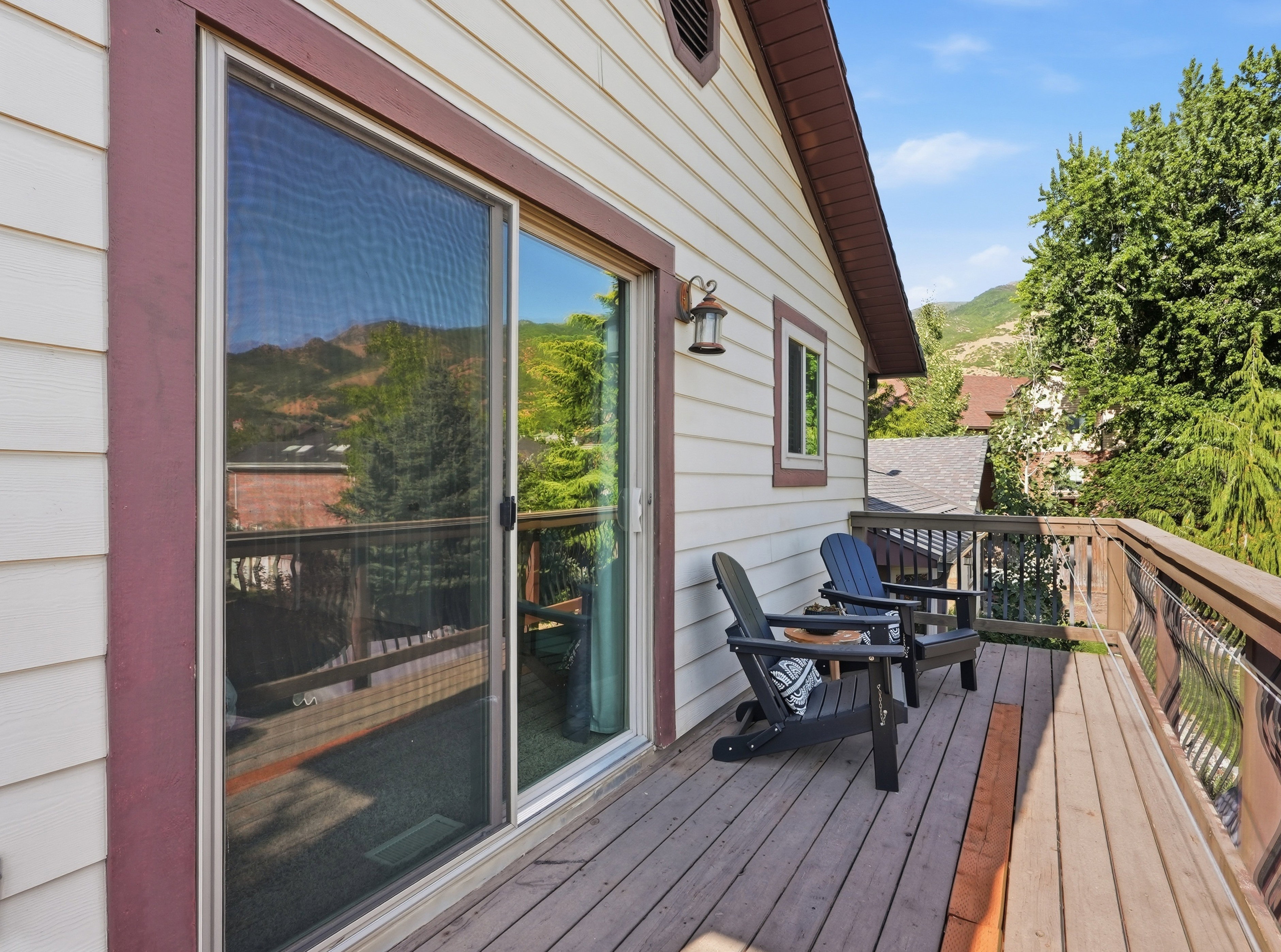 Spacious outdoor deck featuring wood flooring, a sliding glass door, white siding, and mountain scenery