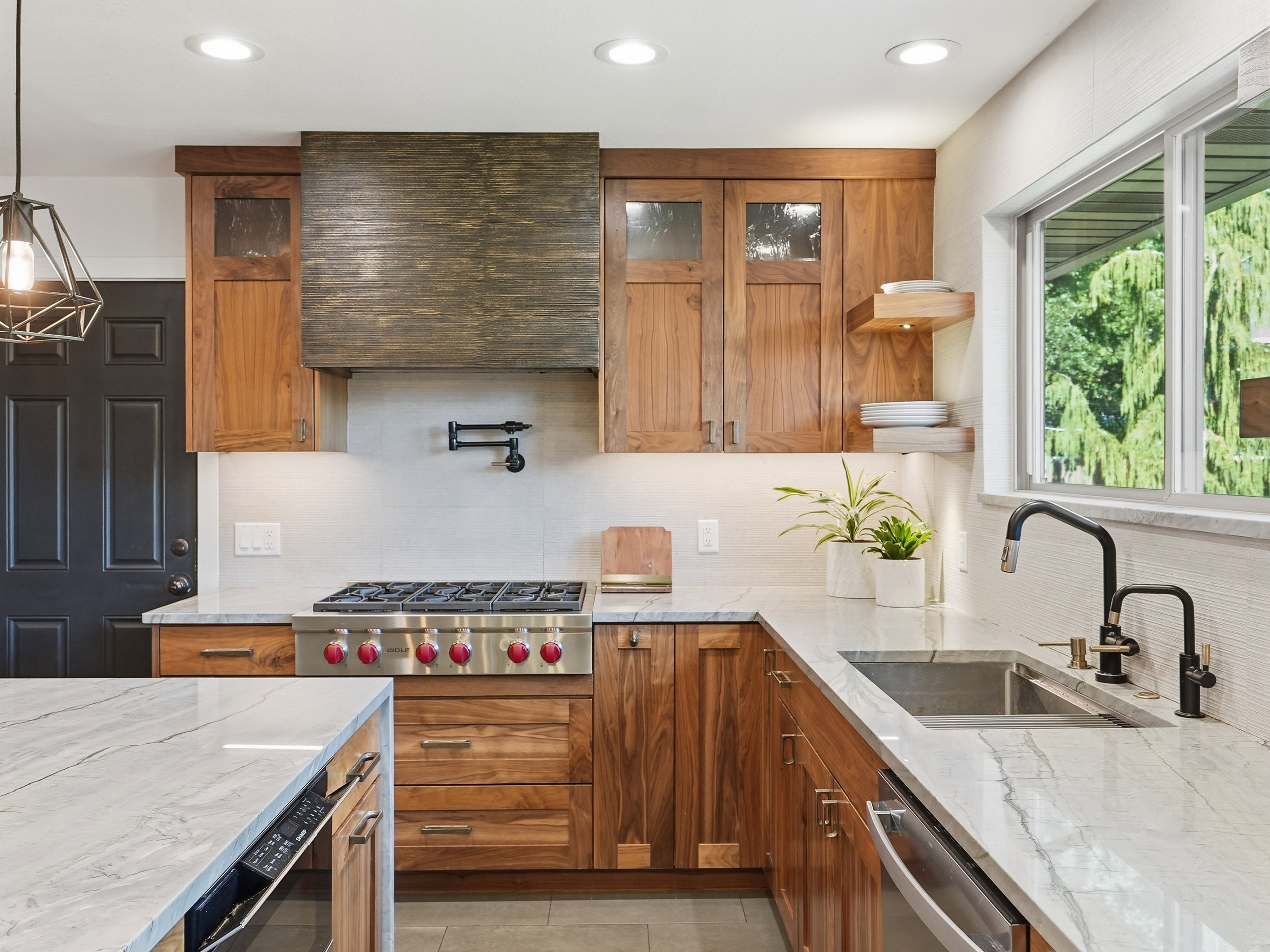 Kitchen featuring custom wood cabinetry, stainless steel range with a pot filler, light-toned countertops, and an undermount sink with a matte black faucet