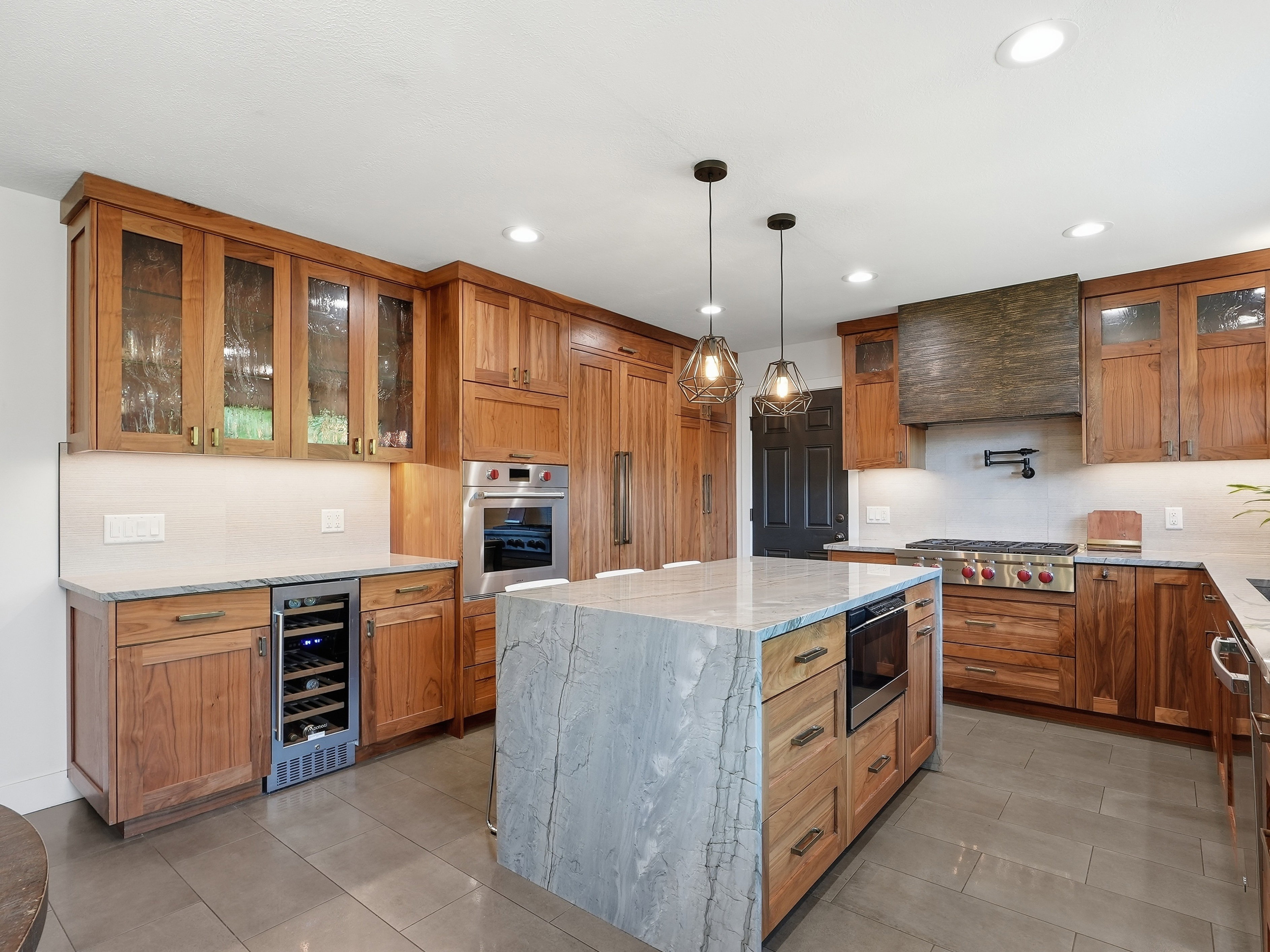 Gourmet kitchen featuring custom wood cabinetry, a large center island with a waterfall countertop, stainless steel appliances, a built-in wine refrigerator, and recessed lighting