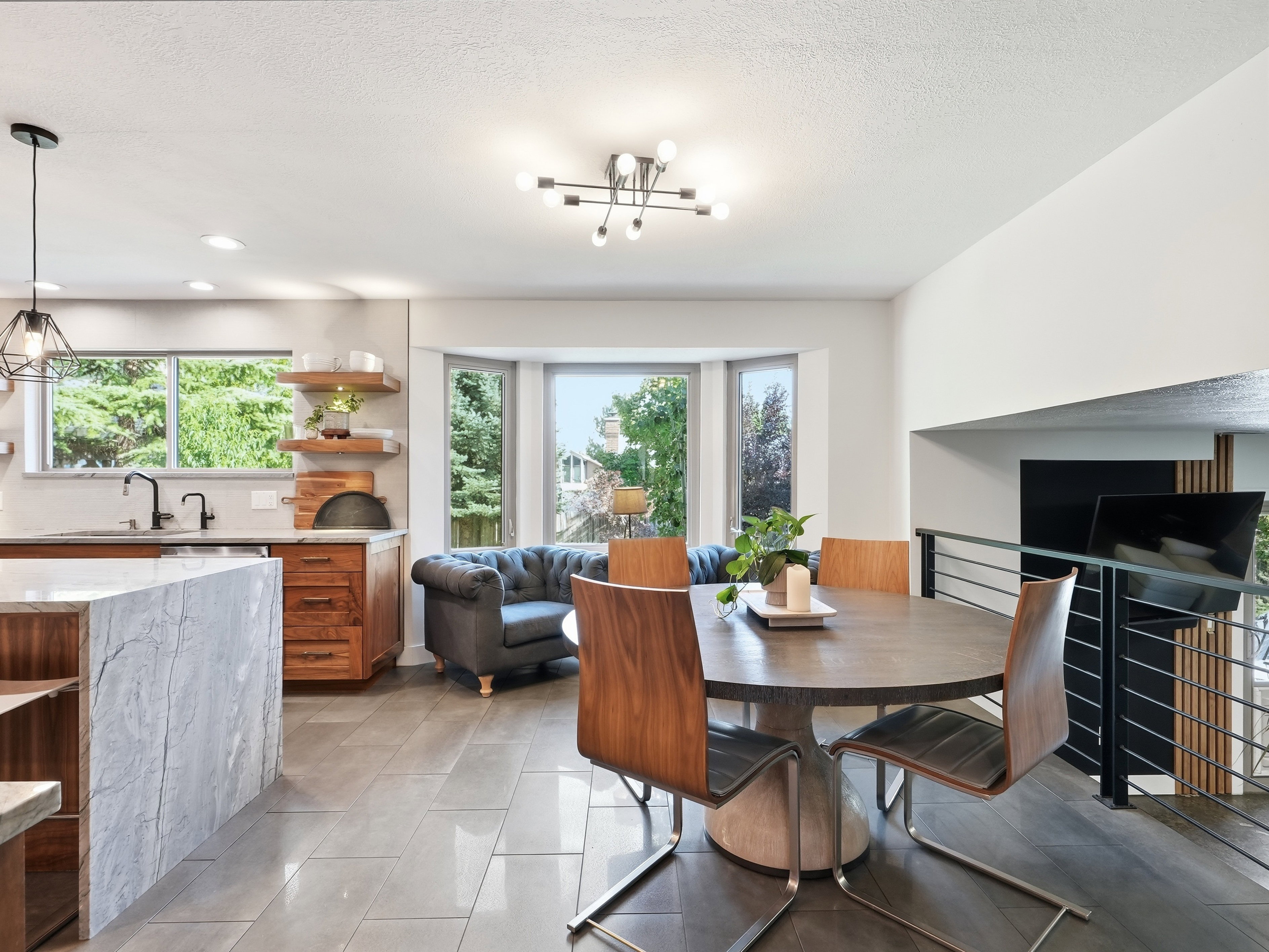 Open-concept kitchen and dining area featuring a waterfall island with stone-finish countertop, wood cabinetry, and a bay window