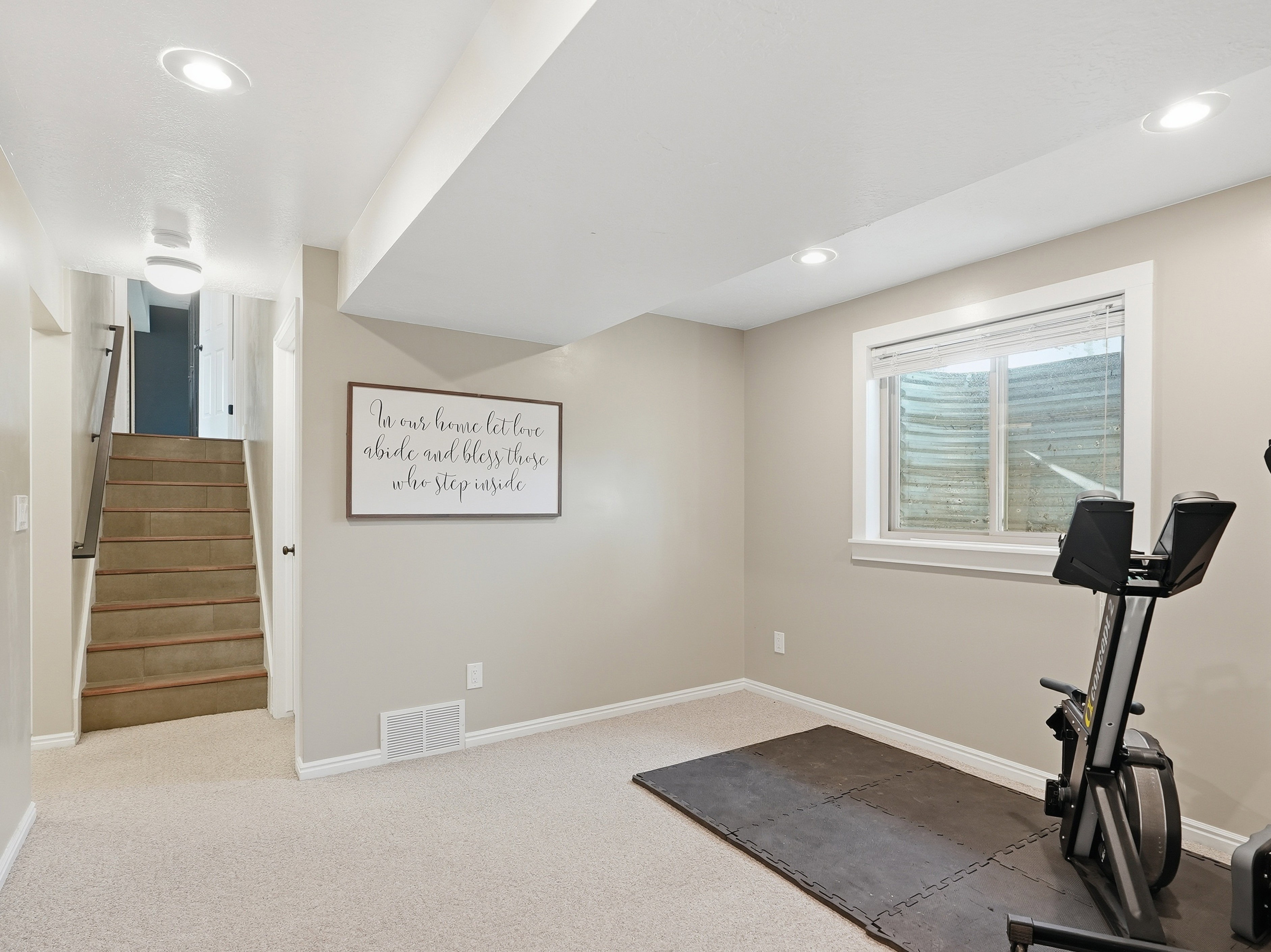 Finished lower-level space featuring recessed lighting, a window, carpet flooring, and a staircase with wood-finish treads