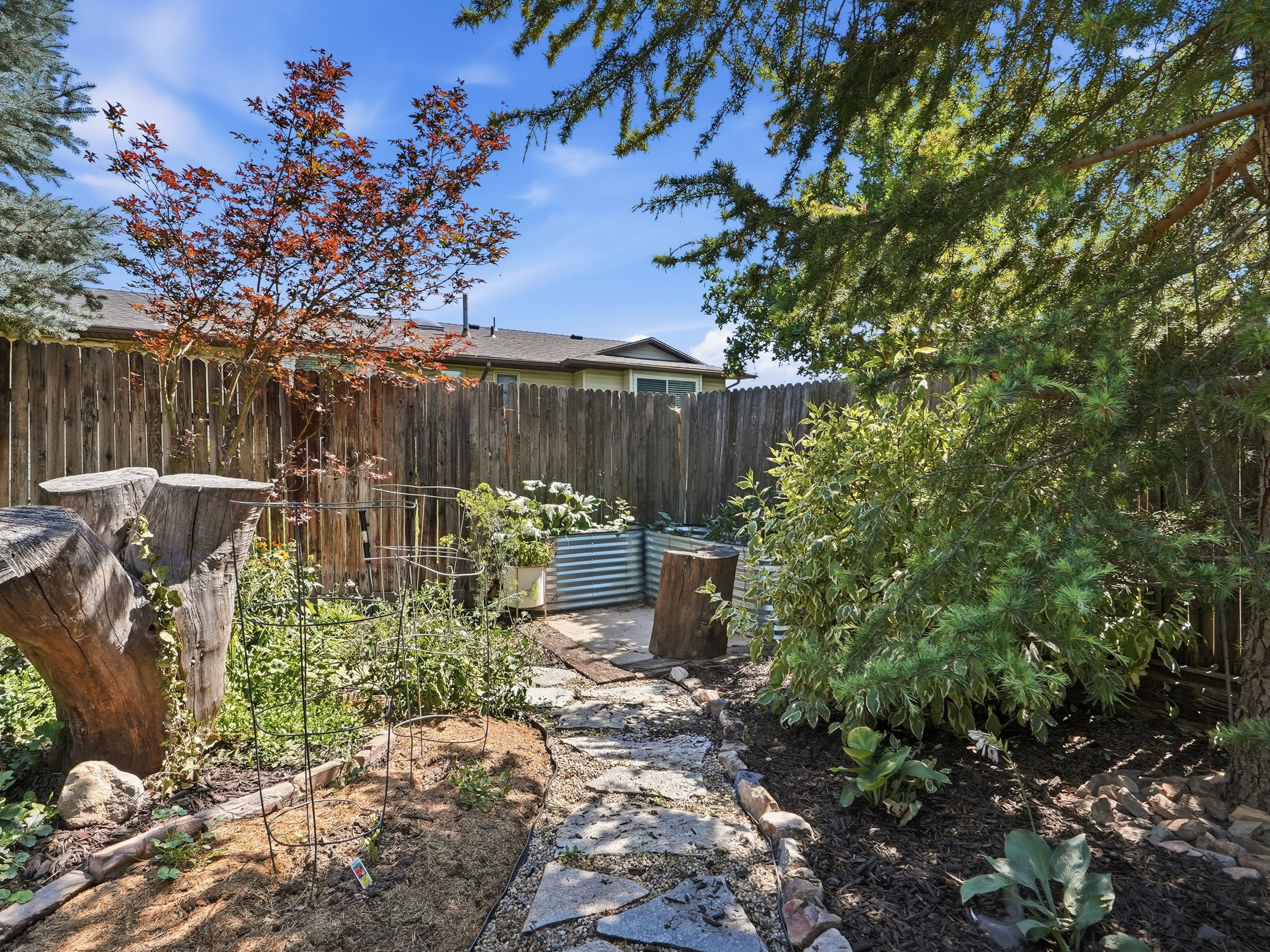 Private backyard space featuring a stone pathway, raised garden beds, wood fencing, and mature trees