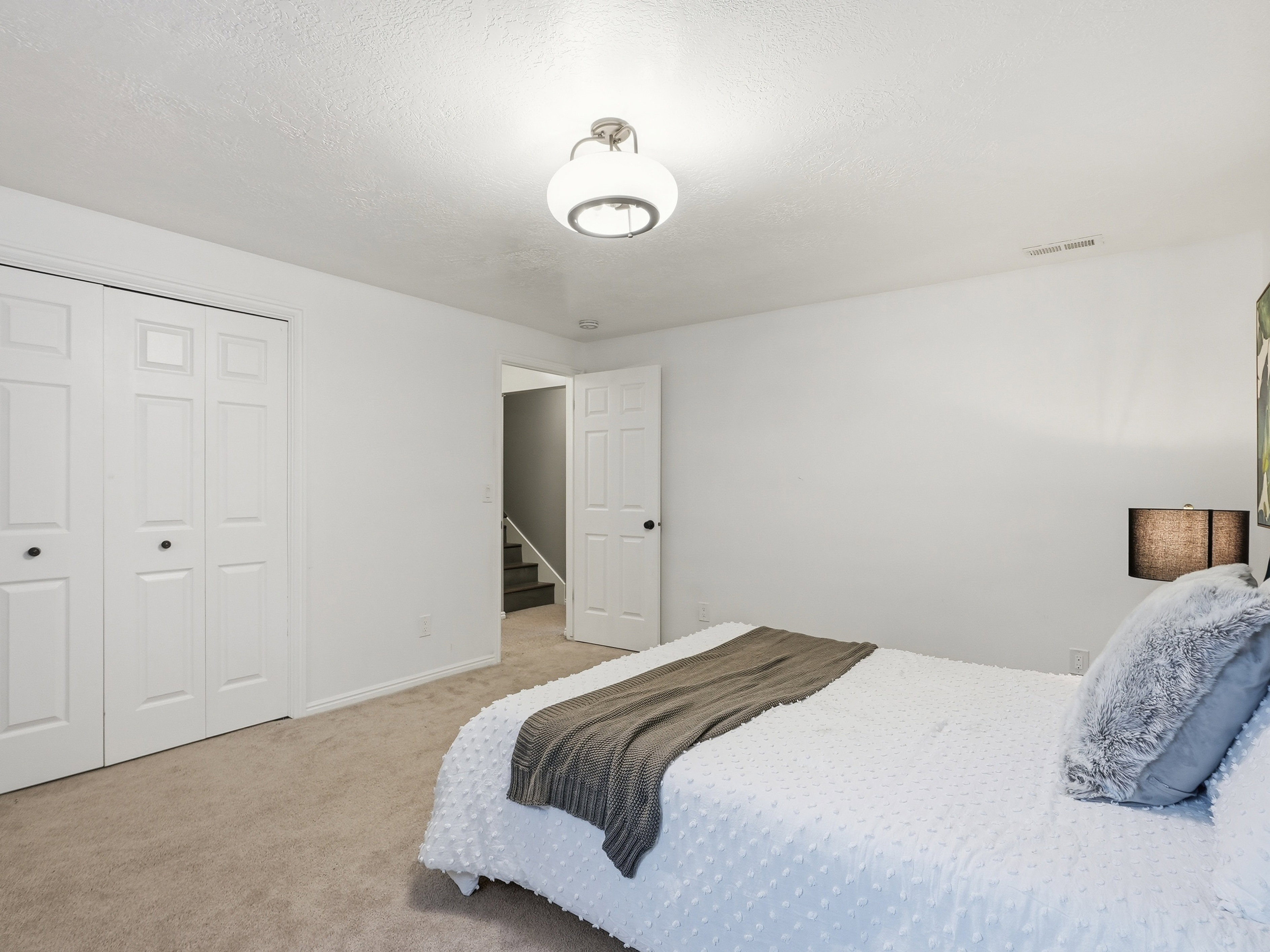 Carpeted room featuring white walls, a flush-mount ceiling light fixture, and bifold closet doors with black hardware