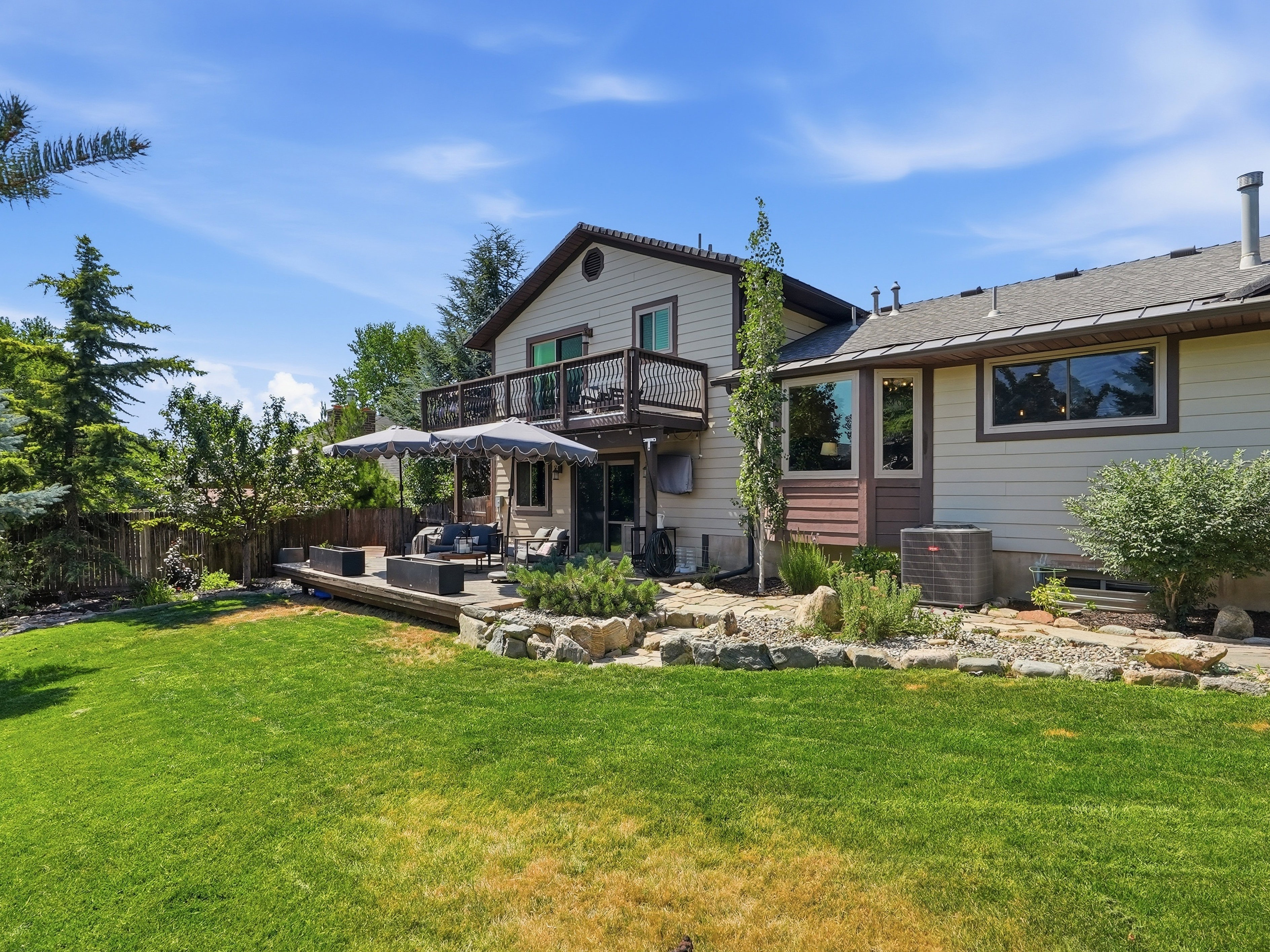 Rear exterior featuring a spacious lawn, multi-level composite deck, and second-story balcony with metal railings