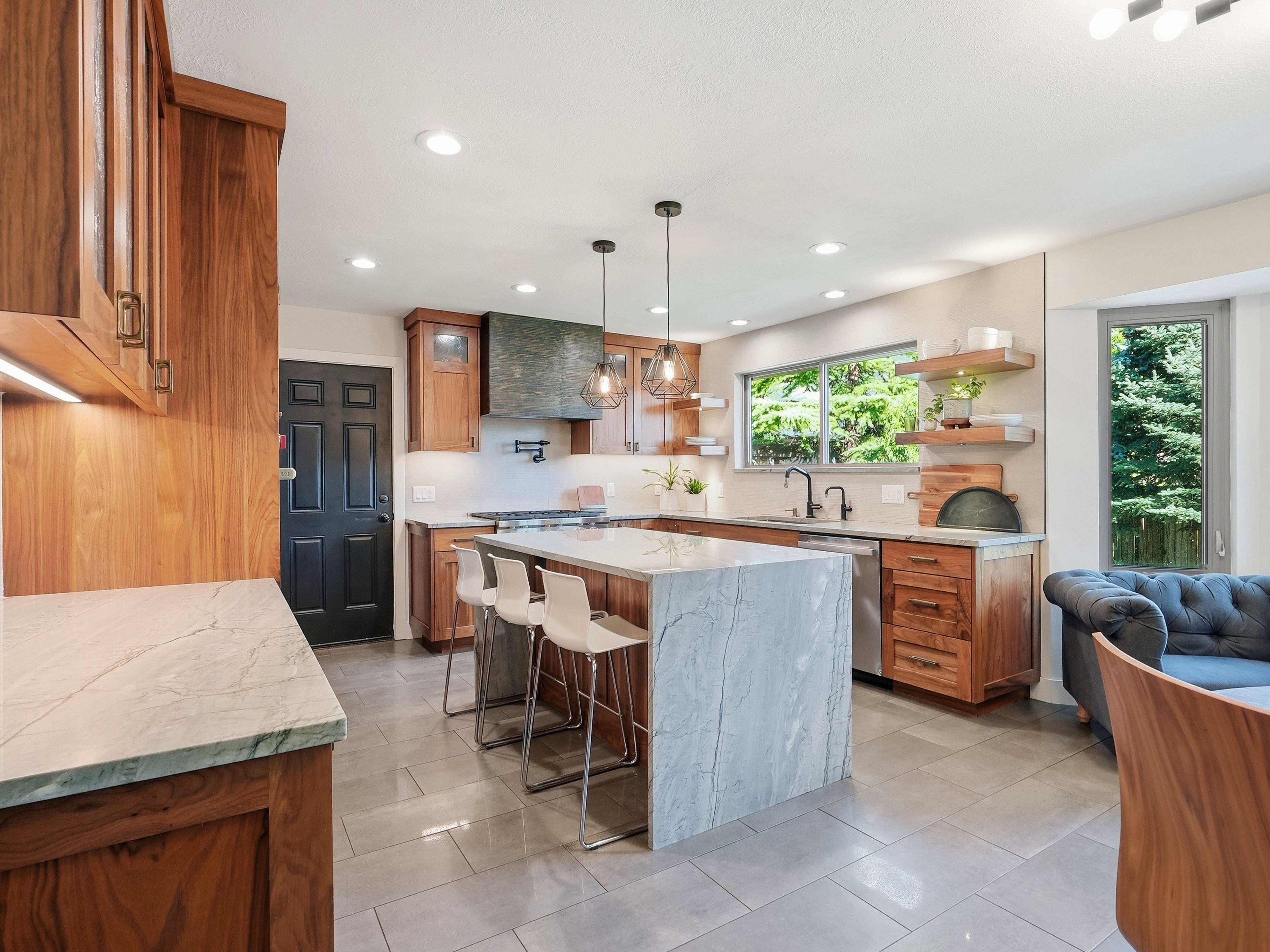Spacious kitchen featuring an oversized island with waterfall countertop, wood-finish cabinetry, stainless steel appliances, recessed lighting, and a large window above the sink