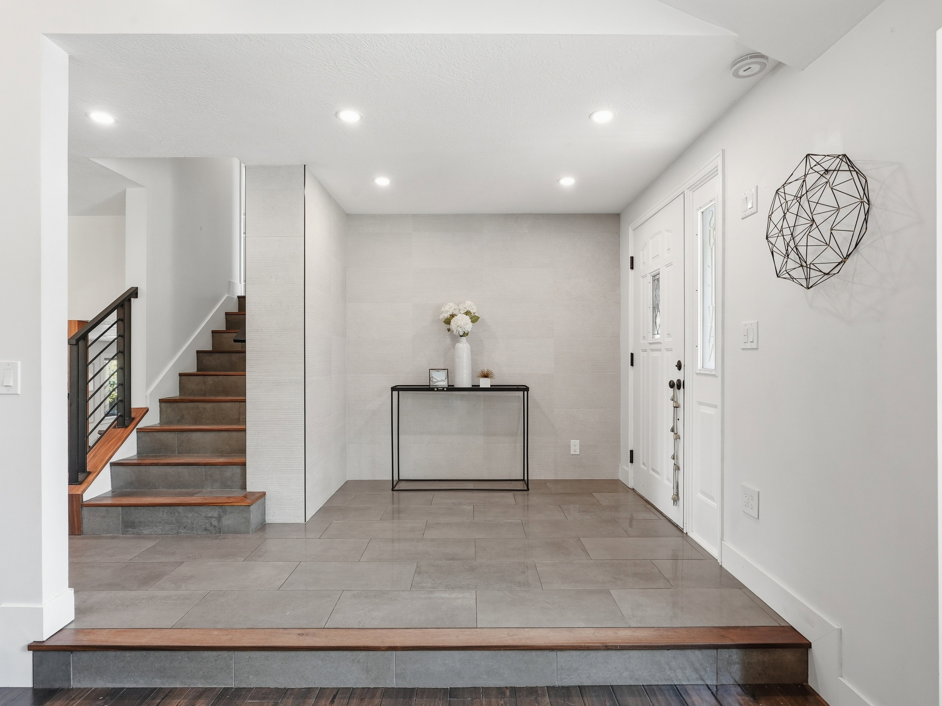Foyer featuring contemporary tile flooring, a two-tone staircase with wood treads and a black metal railing, recessed lighting, and a white paneled entry door with sidelights