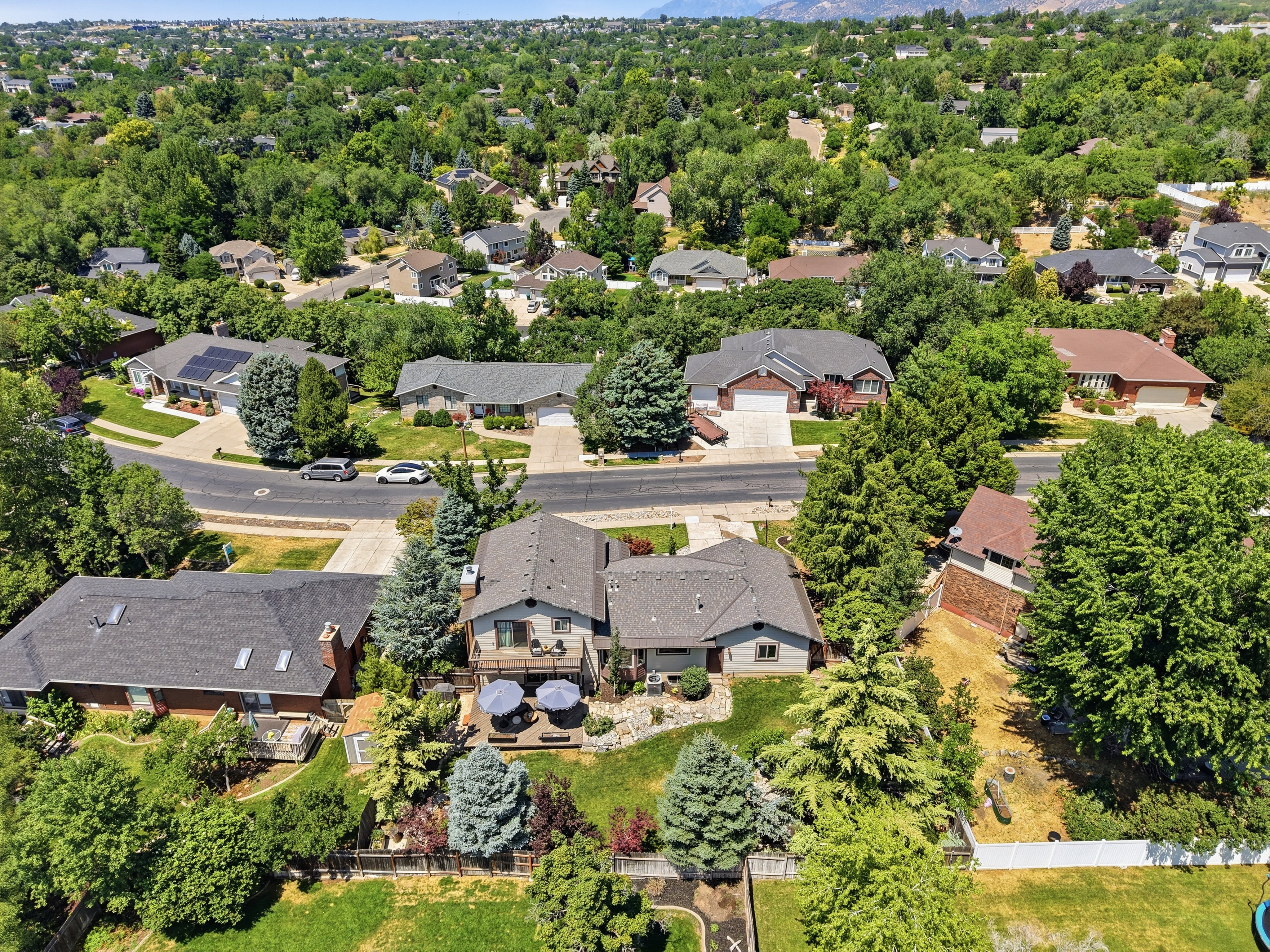 Split-level residence featuring a multi-tier deck with outdoor seating, an upper-level balcony, and a surrounding landscape of mature trees