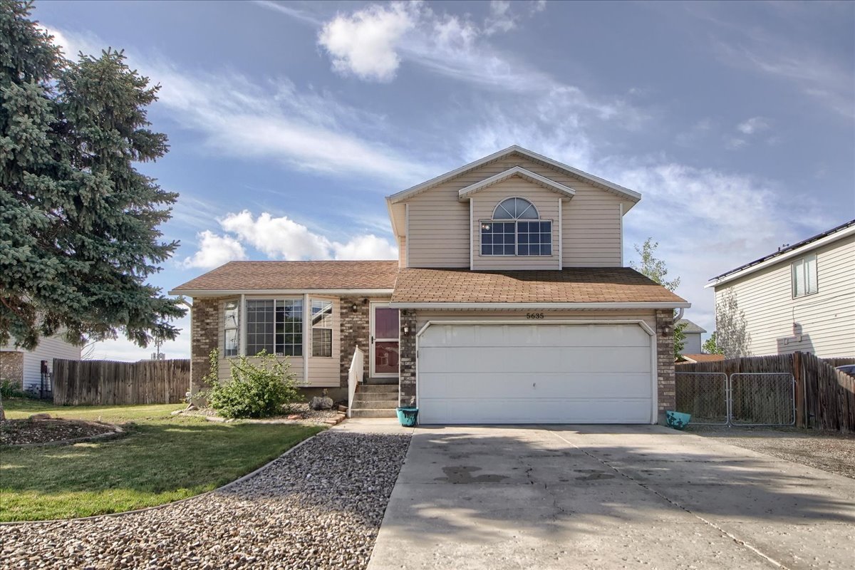Two-story residence featuring a two-car garage, partial brick facade, and tan siding