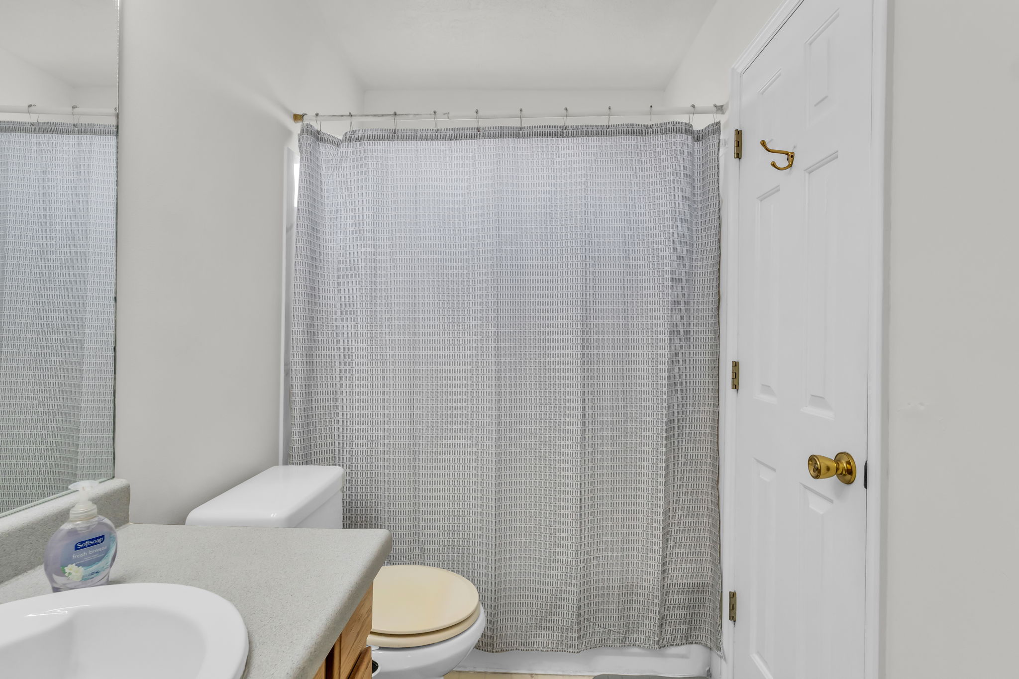 Bathroom featuring a shower with a gray patterned curtain, white panel door with brass hardware, vanity with a light-colored countertop, and an integrated white sink