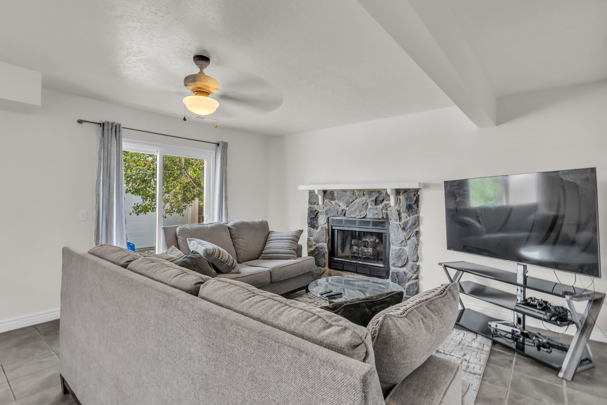 Living area featuring a stone fireplace, dark tile flooring, and a ceiling fan with integrated lighting