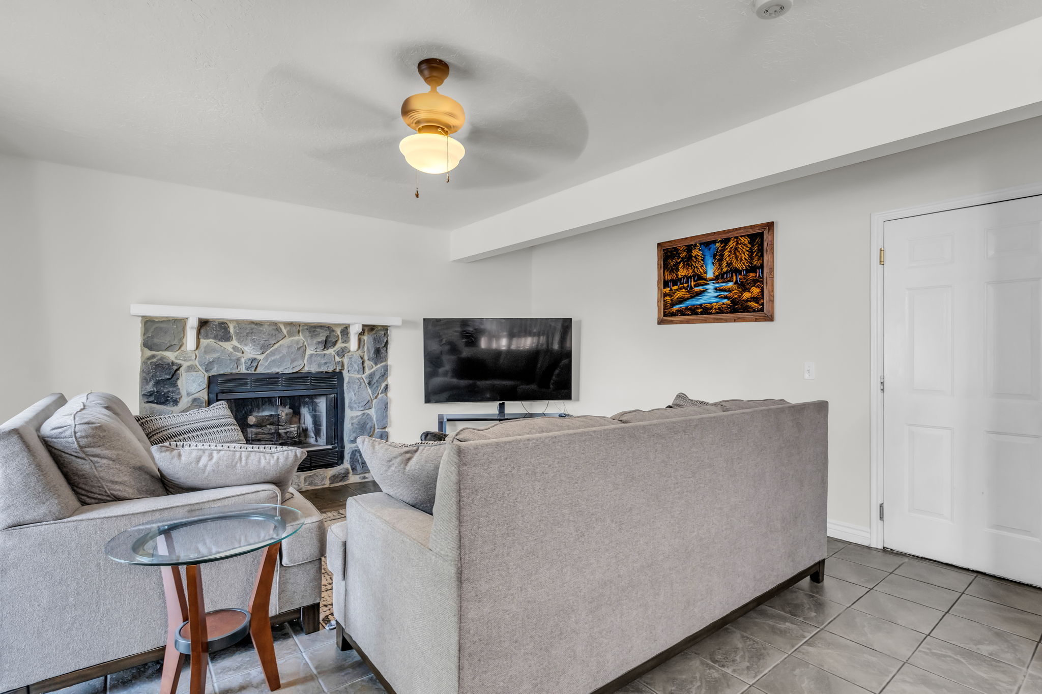 Living area featuring a stone-clad fireplace with a dark hearth, ceiling fan with integrated lighting, and durable tile flooring