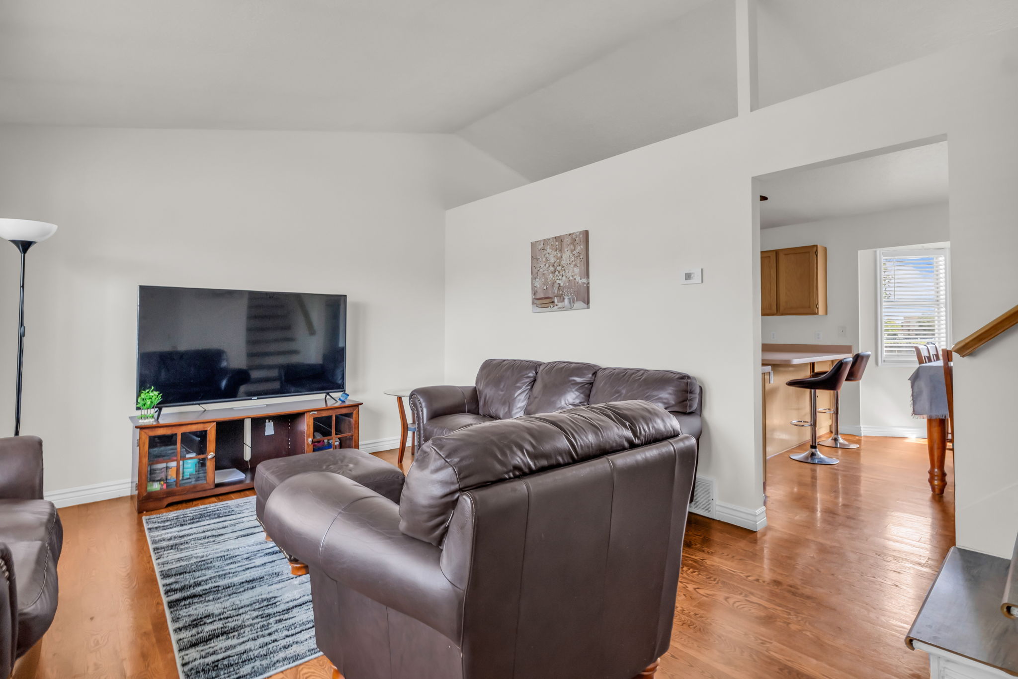 Living area featuring vaulted ceilings, light-toned walls, and wood-finish flooring