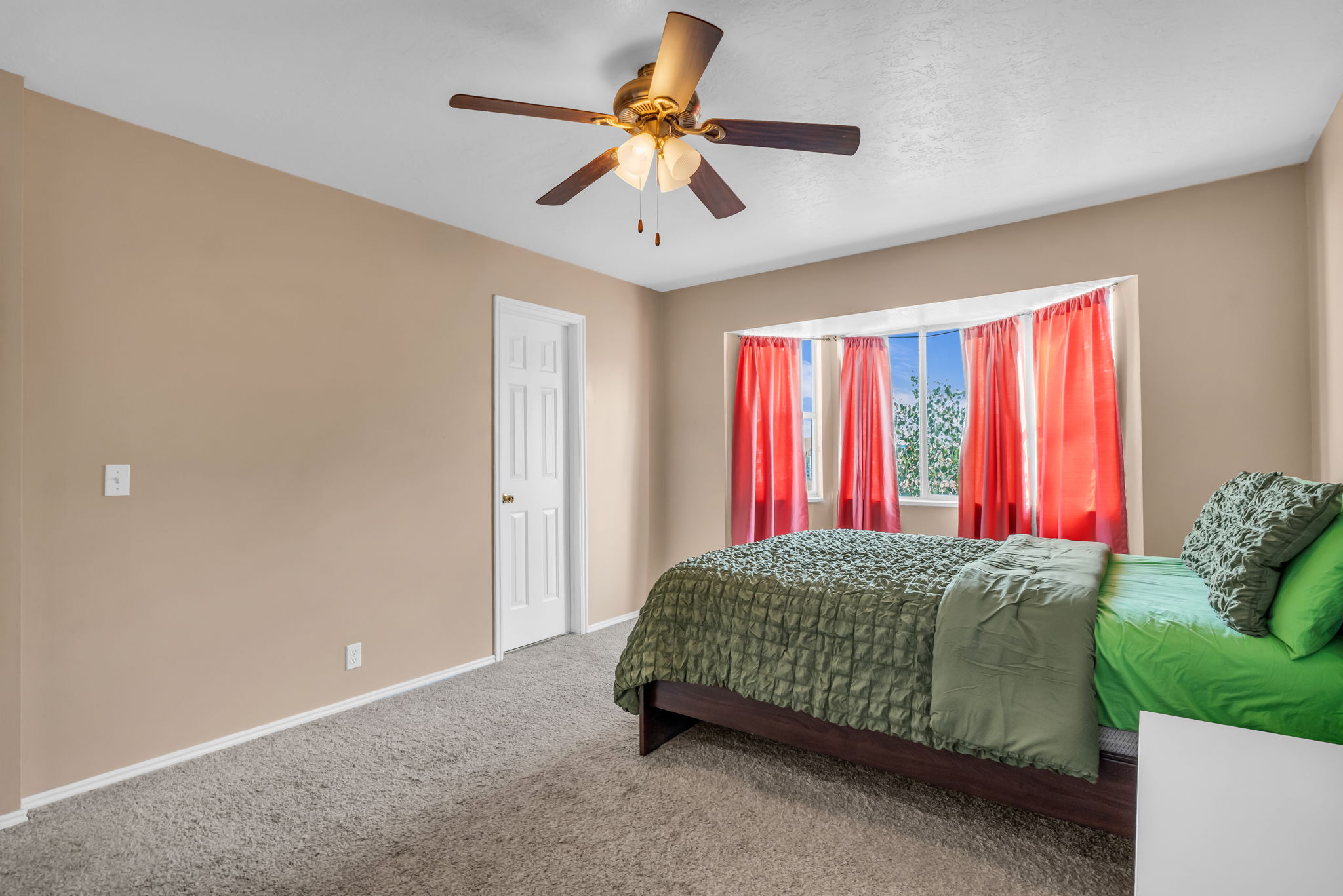 Carpeted room featuring a bay window, ceiling fan with integrated lighting, and a paneled white door
