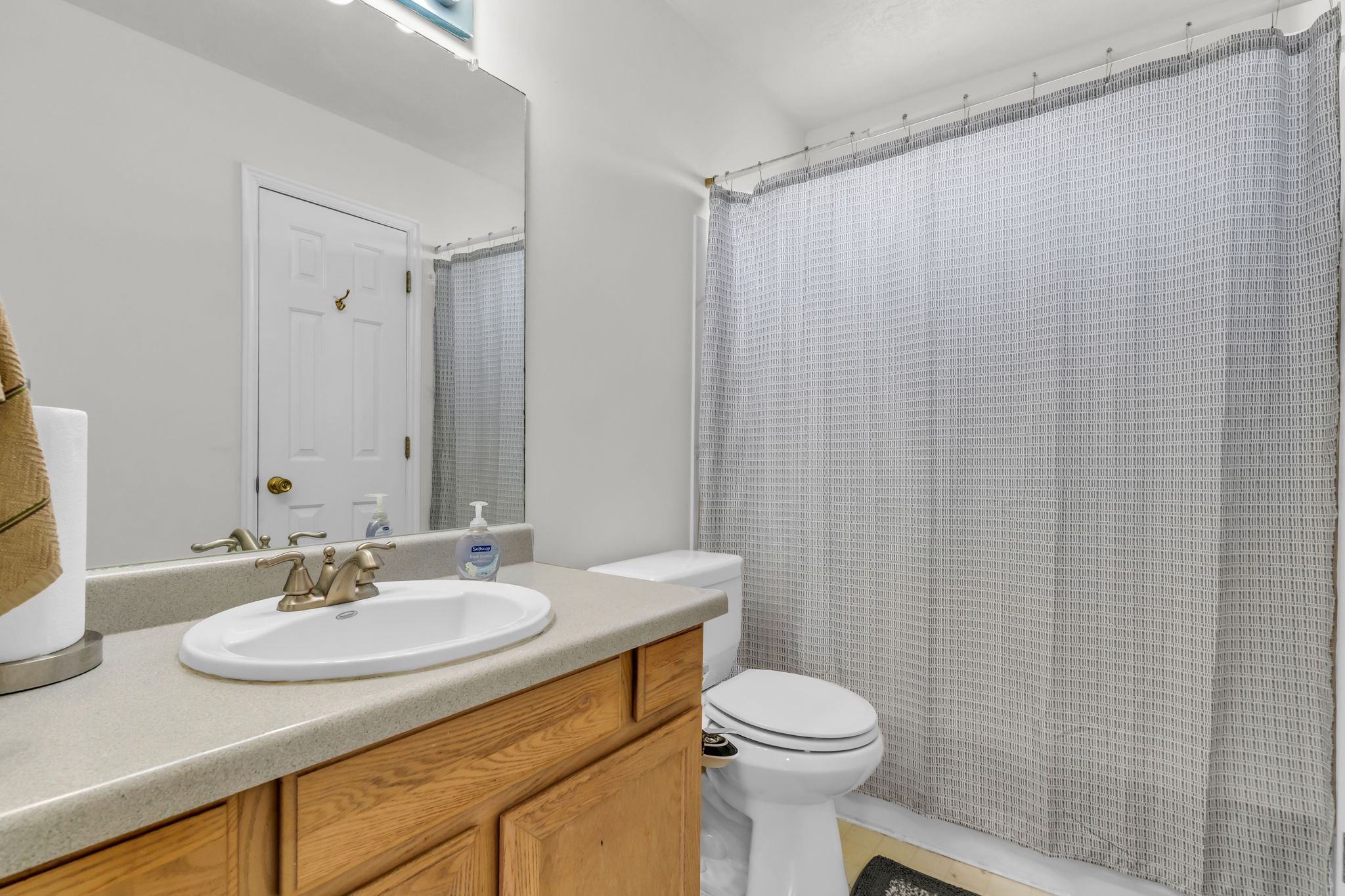 Bathroom featuring a wood-finish vanity with a light-toned countertop, an oval undermount sink, and a mirrored wall