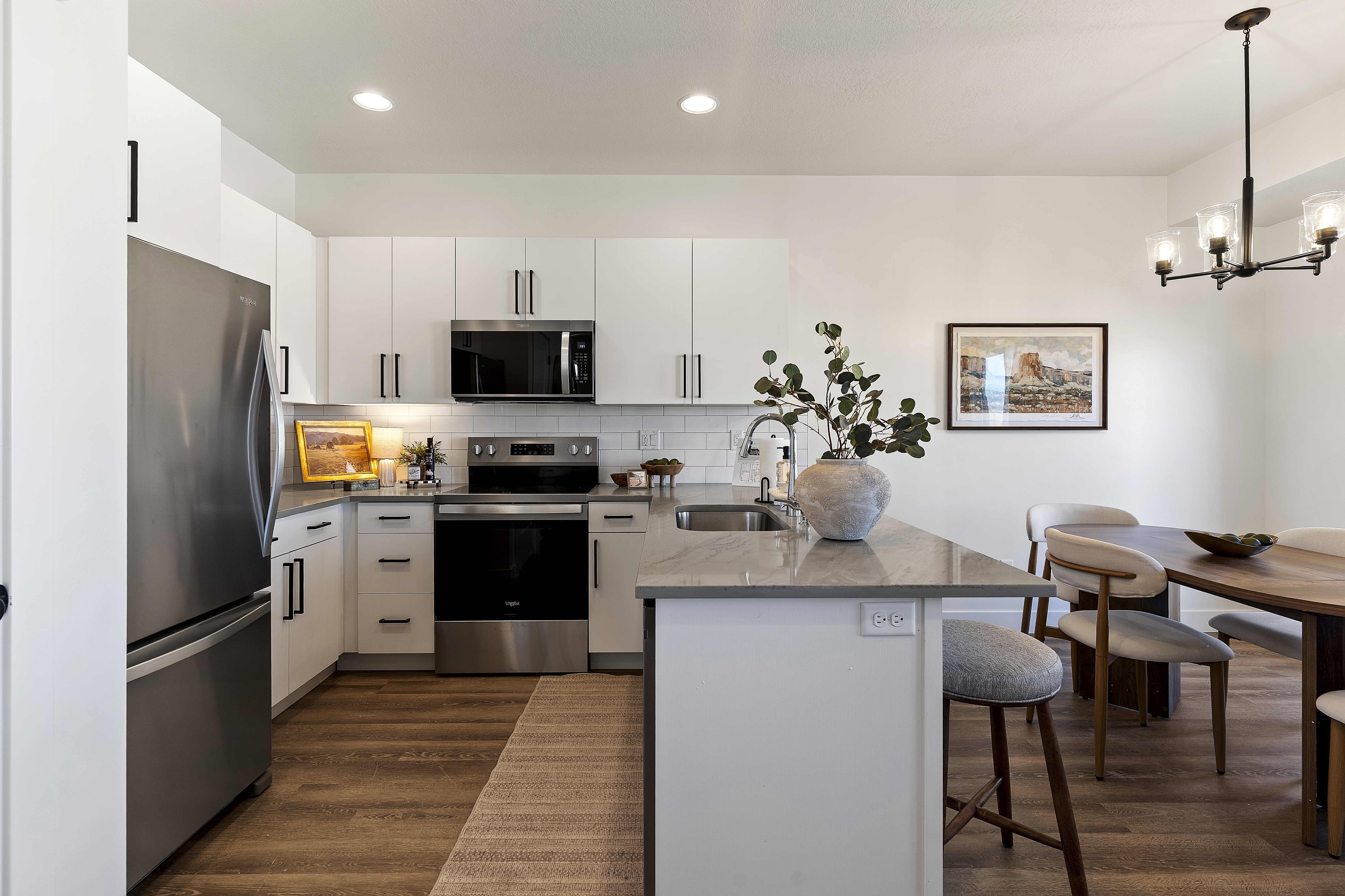 Kitchen and dining area featuring white cabinetry with matte black hardware, stainless steel appliances, a subway tile backsplash, light-toned countertops, and wood-finish flooring