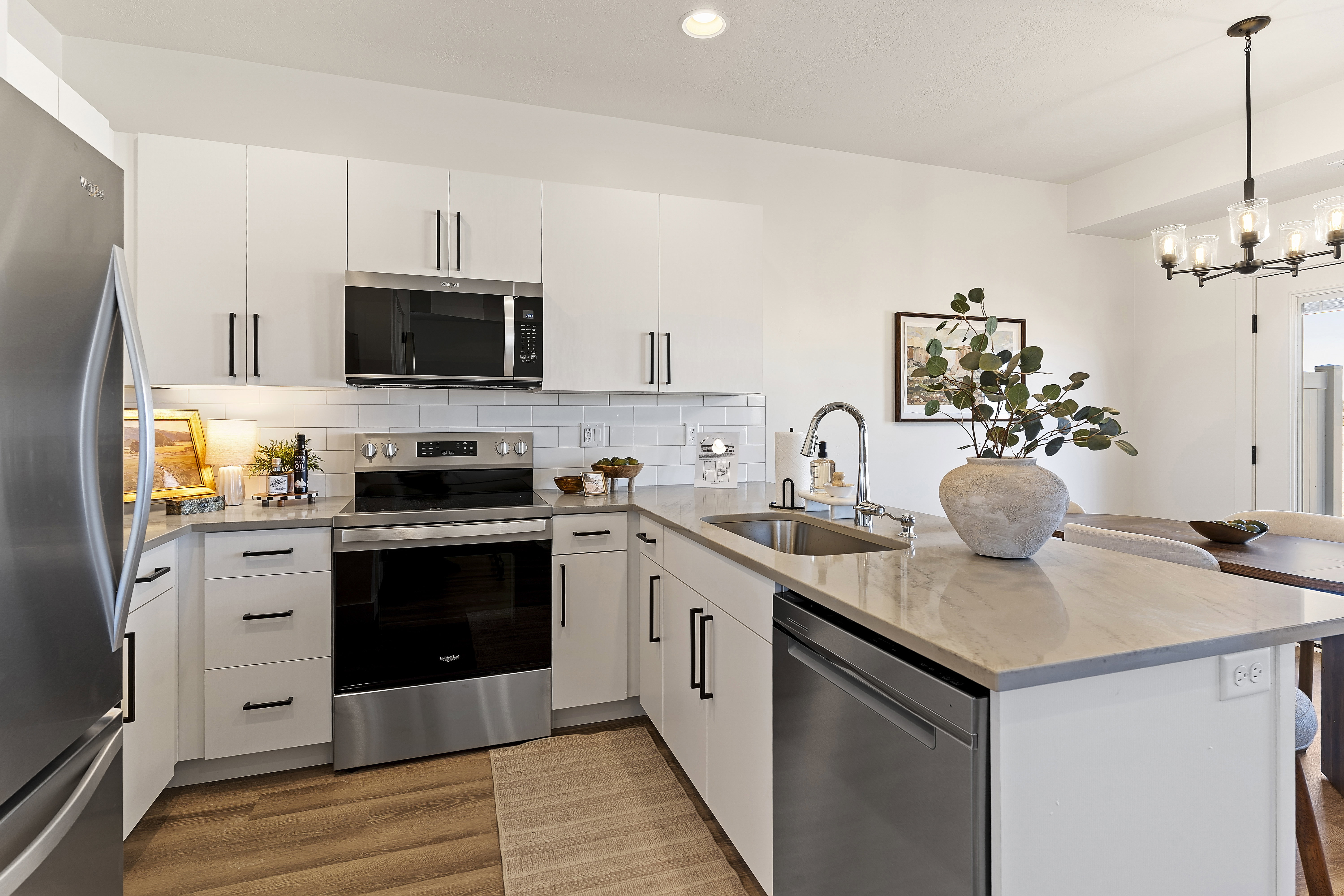 Modern kitchen featuring white cabinetry, stainless steel appliances, a subway tile backsplash, a kitchen island with an undermount sink, and wood-finish flooring