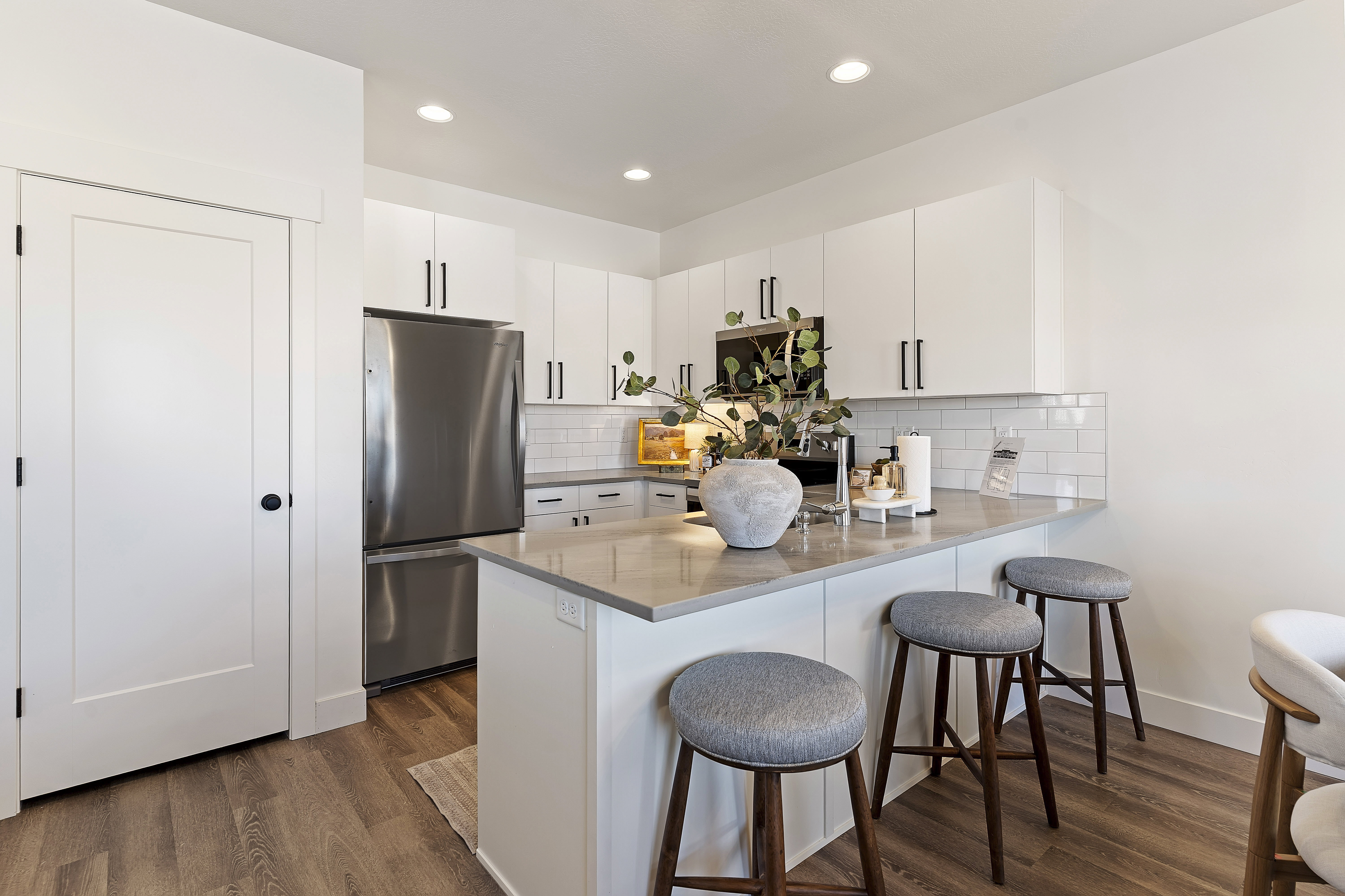 Modern kitchen featuring an island with counter seating, stainless steel appliances, white subway tile backsplash, white flat-panel cabinetry with dark hardware, and wood-finish flooring