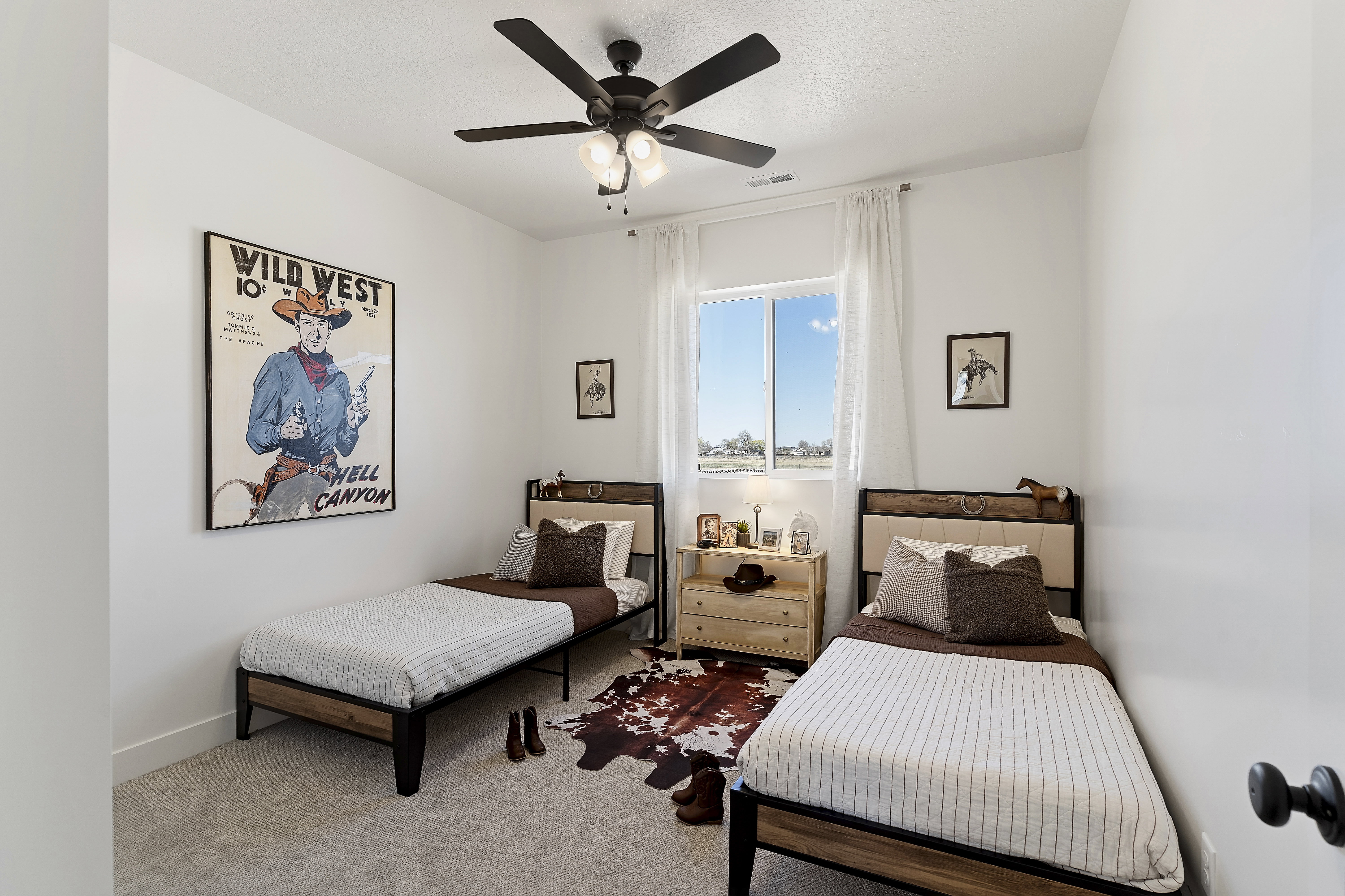 Bright bedroom featuring a large window with white sheer curtains, a dark ceiling fan with integrated lighting, and light-colored wall-to-wall carpeting