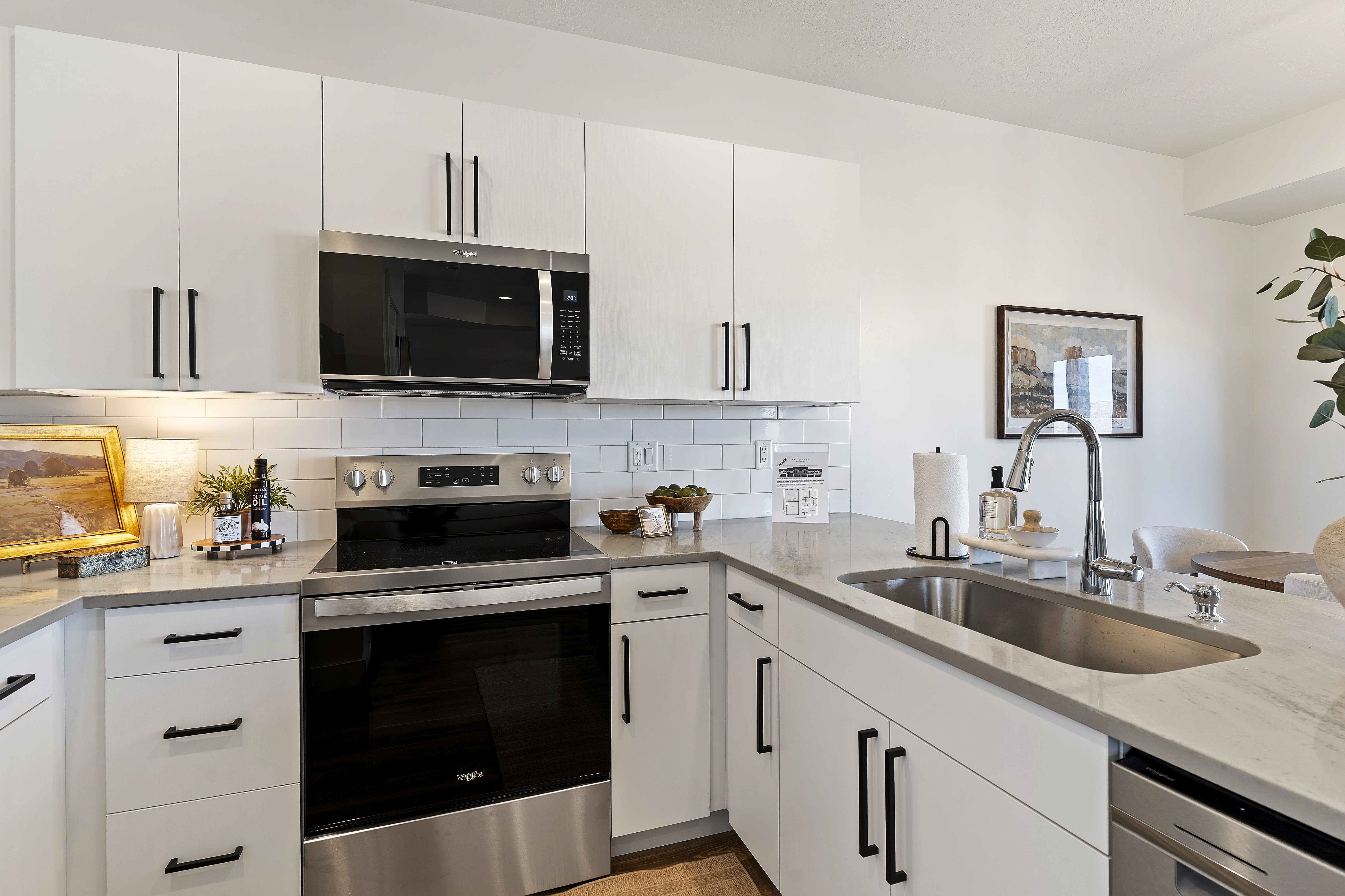 Modern kitchen featuring white cabinetry with matte black hardware, stainless steel appliances, a subway tile backsplash, light grey countertops, and an undermount sink with a gooseneck faucet