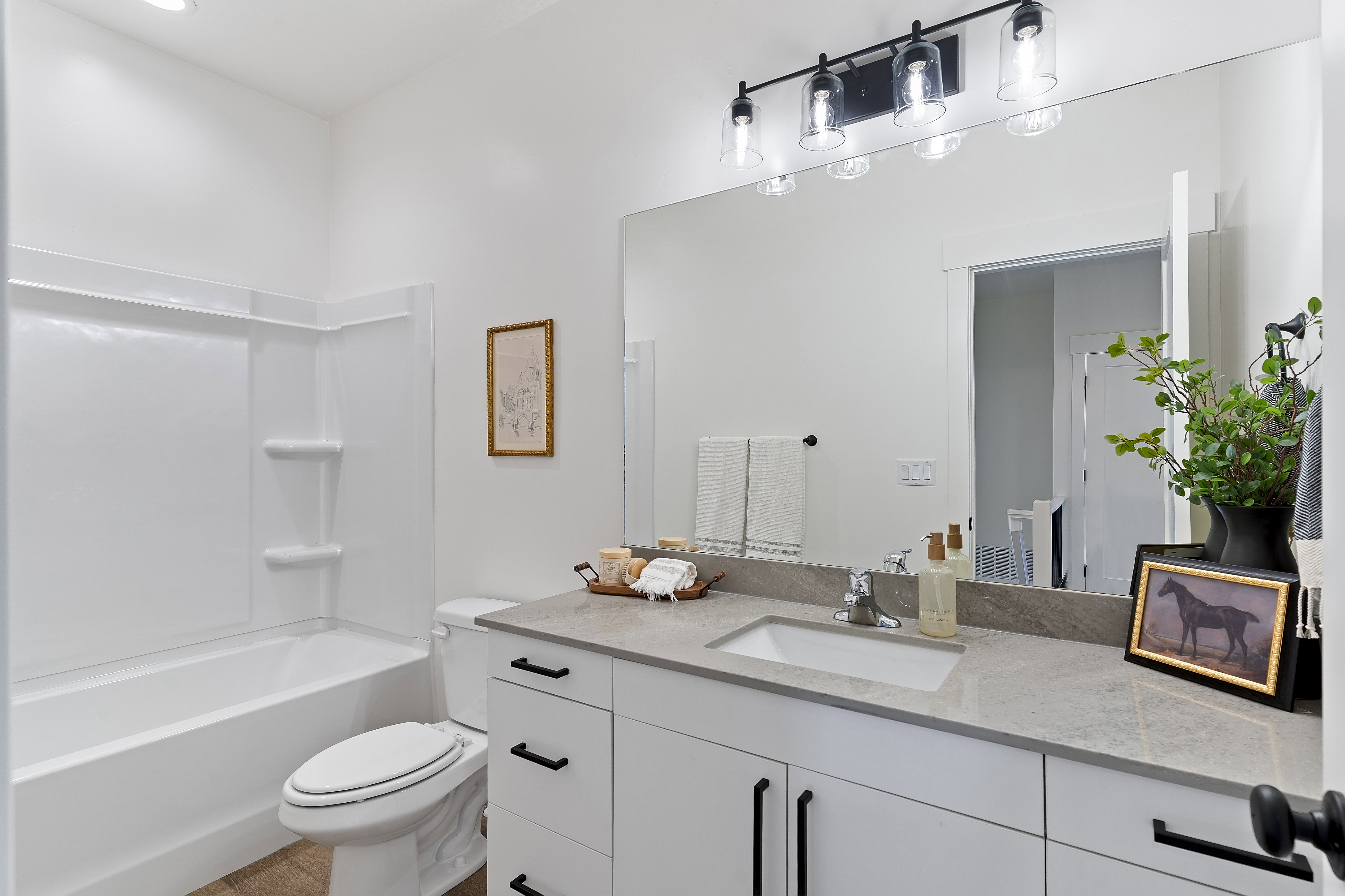 Bathroom featuring a white vanity with matte black hardware, a grey countertop, a rectangular undermount sink, a large wall mirror, and a four-light vanity fixture