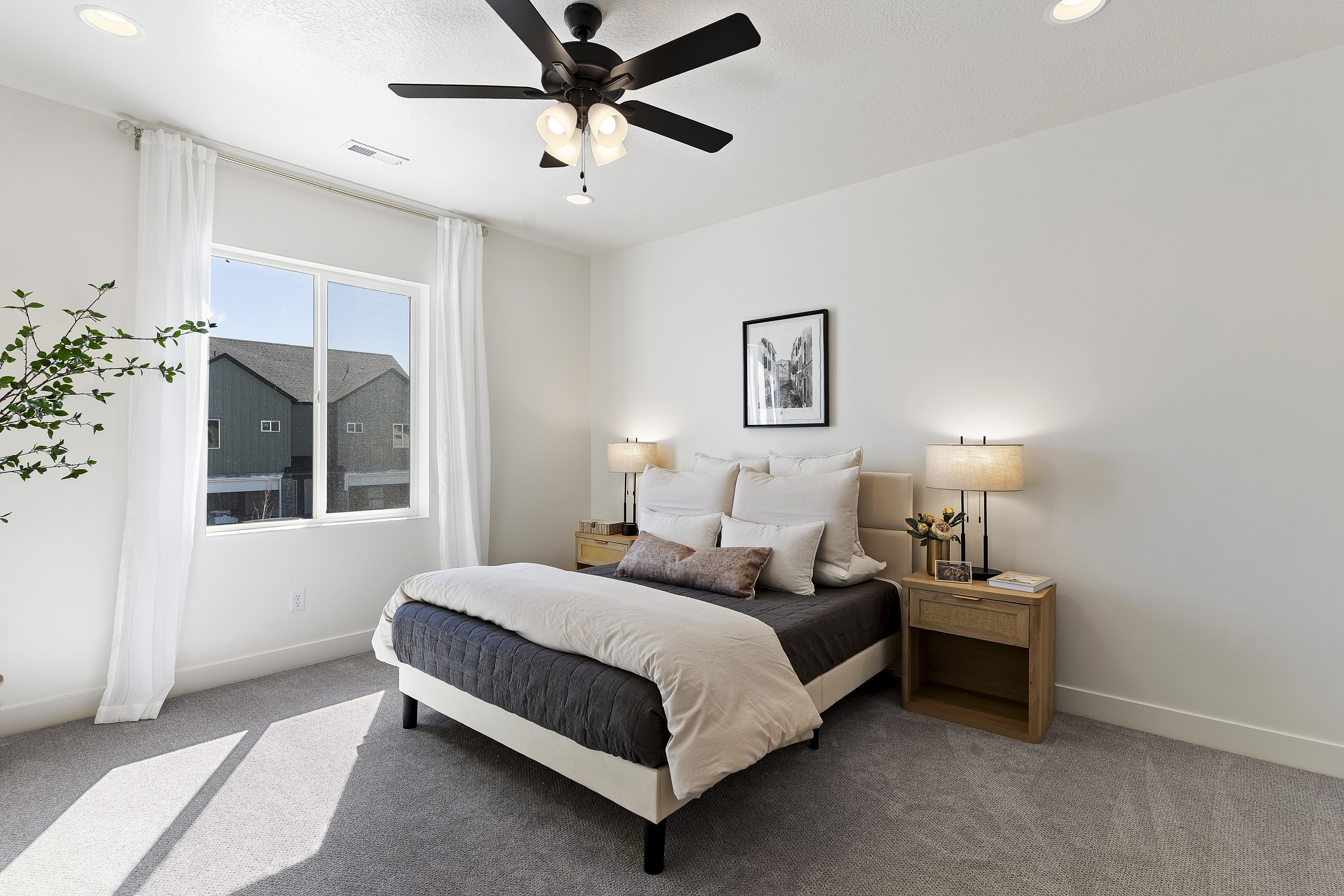 Carpeted bedroom featuring a large window with white curtains, a ceiling fan with integrated lighting, and recessed ceiling lights