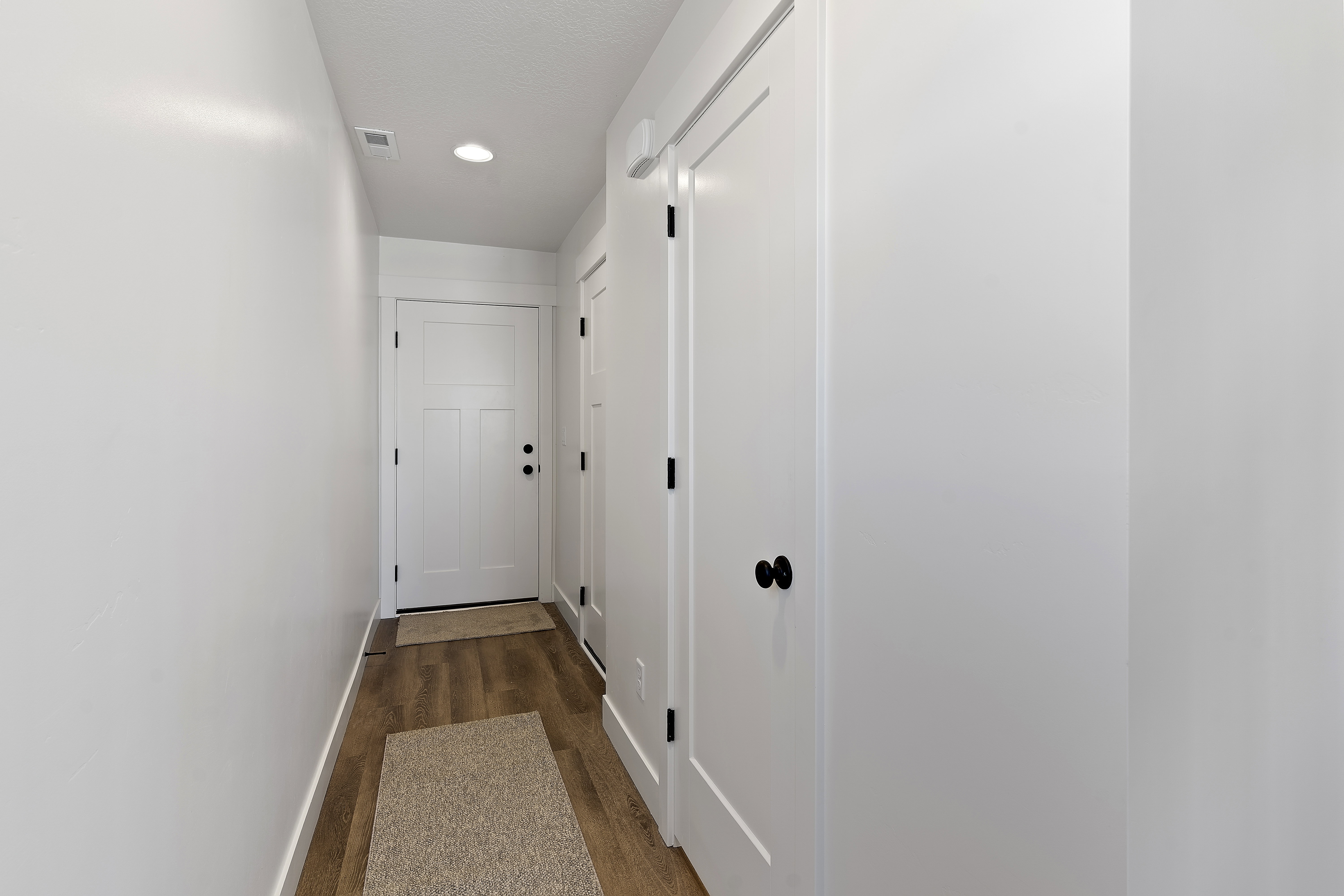 Entryway featuring a white paneled door with matte black hardware, wood-finish flooring, recessed lighting, and crisp white walls
