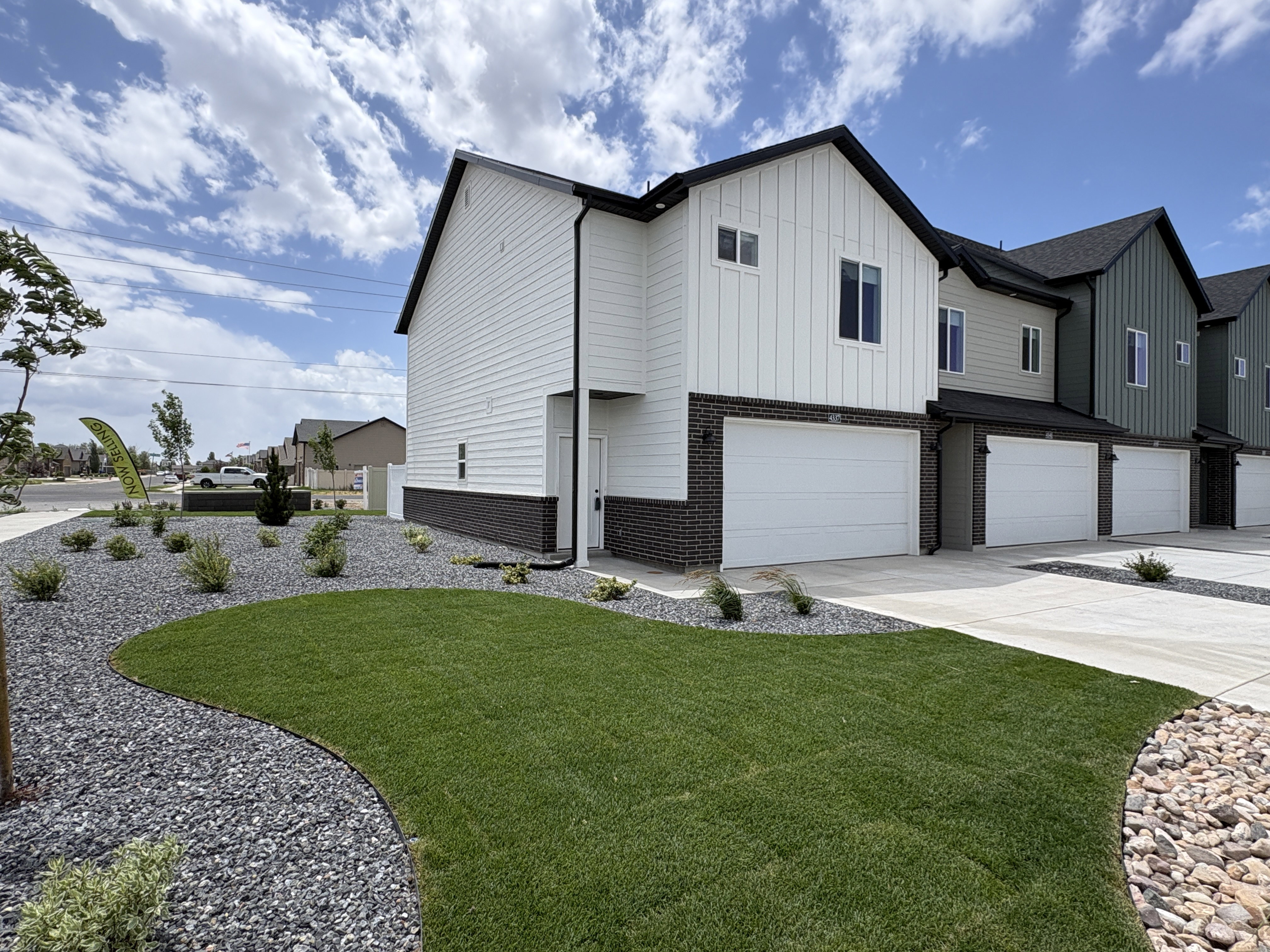 Modern townhome exterior featuring vertical and horizontal white siding, dark brick accents, and a two-car garage
