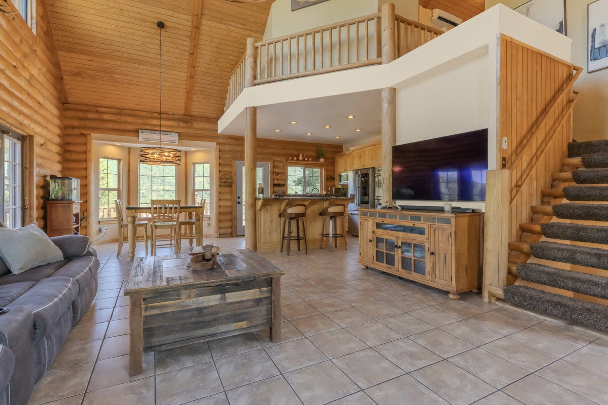 Open-concept living area with vaulted wood plank ceilings, exposed log walls, and large windows