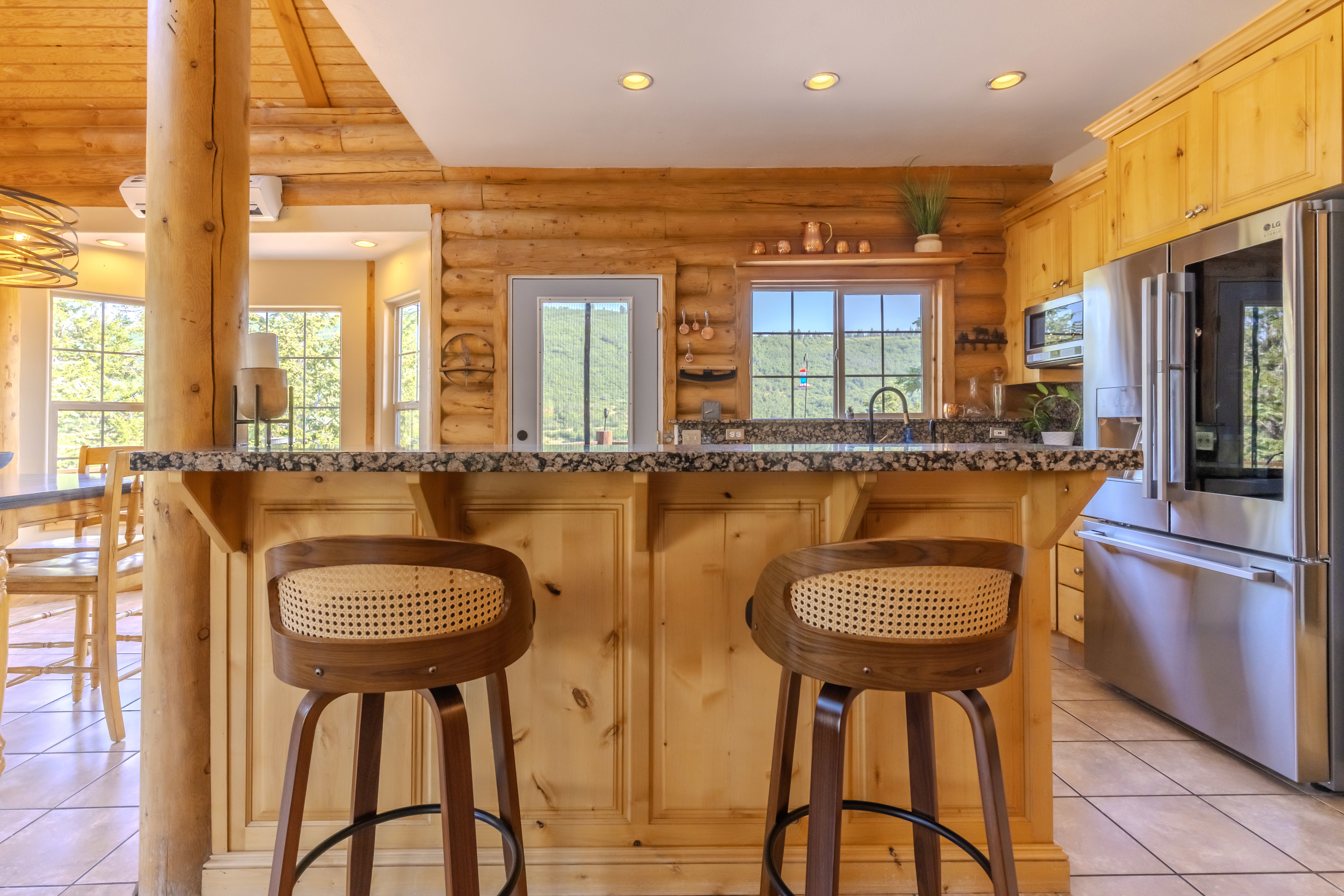 Kitchen featuring a breakfast bar with stone-finish countertop, light wood cabinetry, stainless steel appliances, and a window above the sink